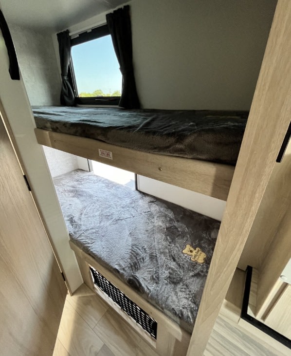 Inside an RV rental, showing cozy double bunk beds with dark blankets and a window. Ideal for families.. Winnebago Minnie Winnie 2022