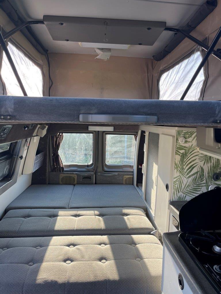 View inside an RV rental pop-top camper, showing a lower convertible bed, upper loft bed, and a compact kitchen.. Ford E350 2008