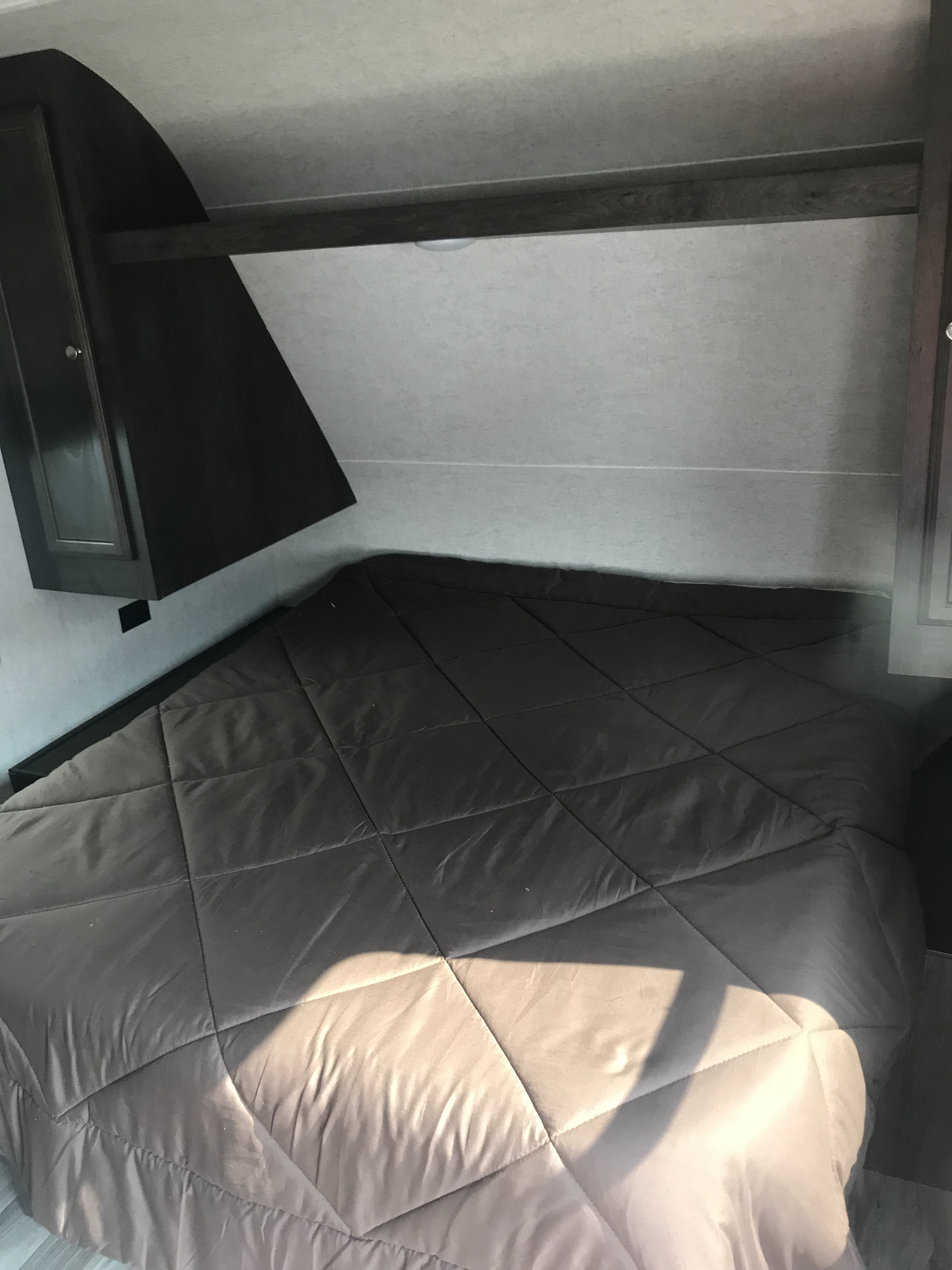Cozy RV rental bedroom featuring a quilted comforter, dark overhead cabinets, and a shelf, illuminated by natural light.. Starcraft Mossy Oak 2019