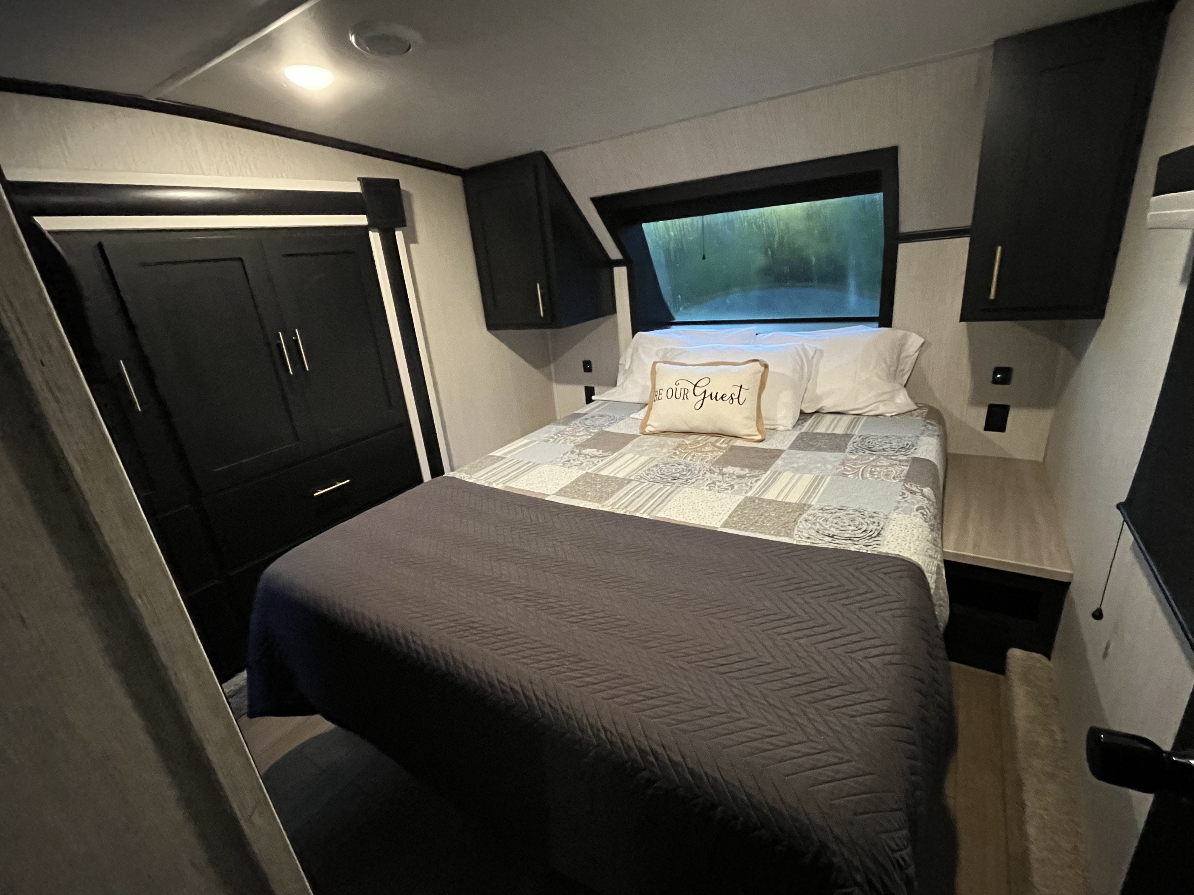 Spacious RV rental bedroom featuring a comfy bed with a "Be Our Guest" pillow, built-in storage, and a scenic window.. Forest River Wildcat 2022