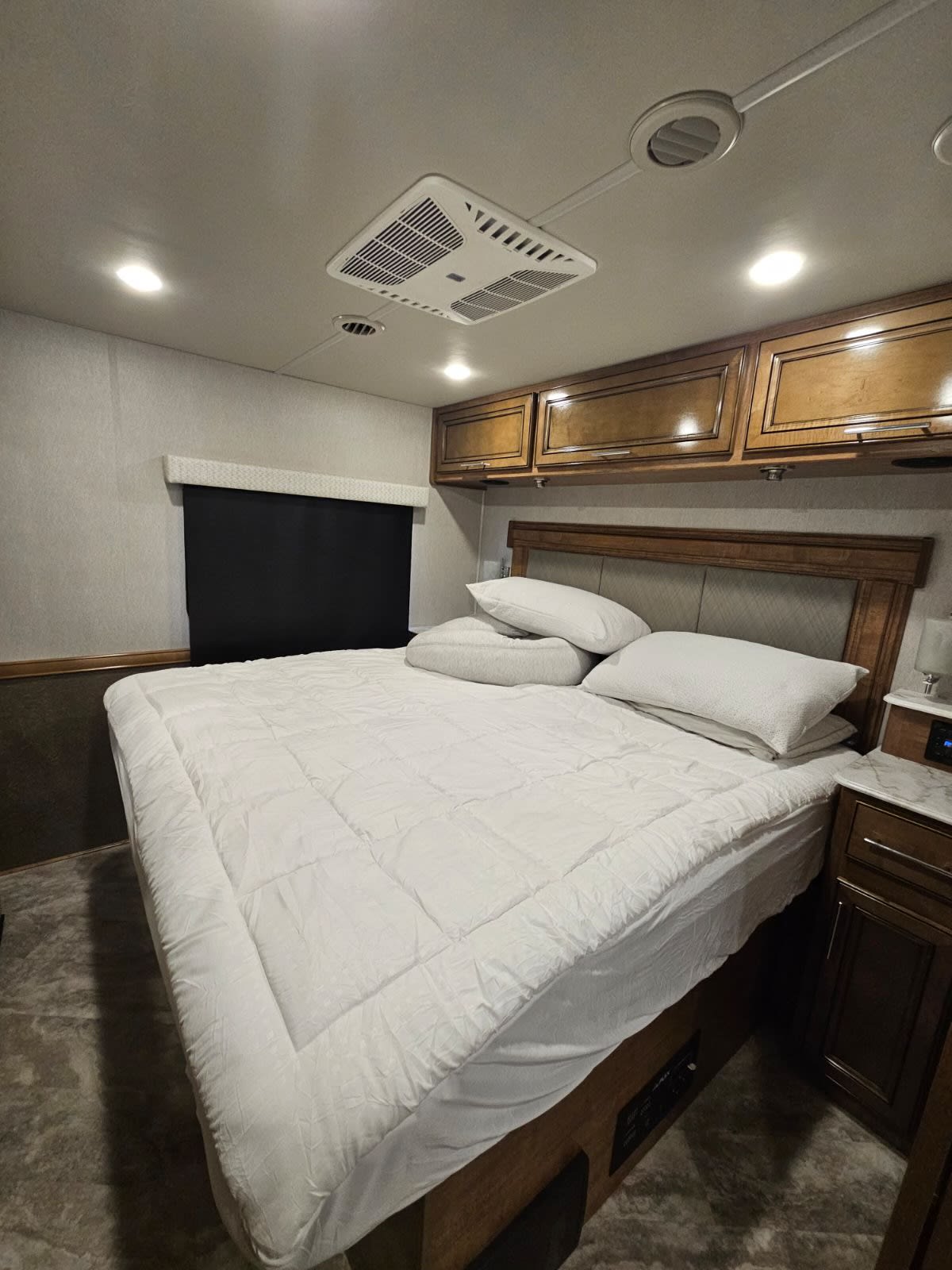 Queen bed in a well-appointed RV rental bedroom, featuring overhead cabinets, ample lighting, and an AC unit.. Fleetwood flex 2023