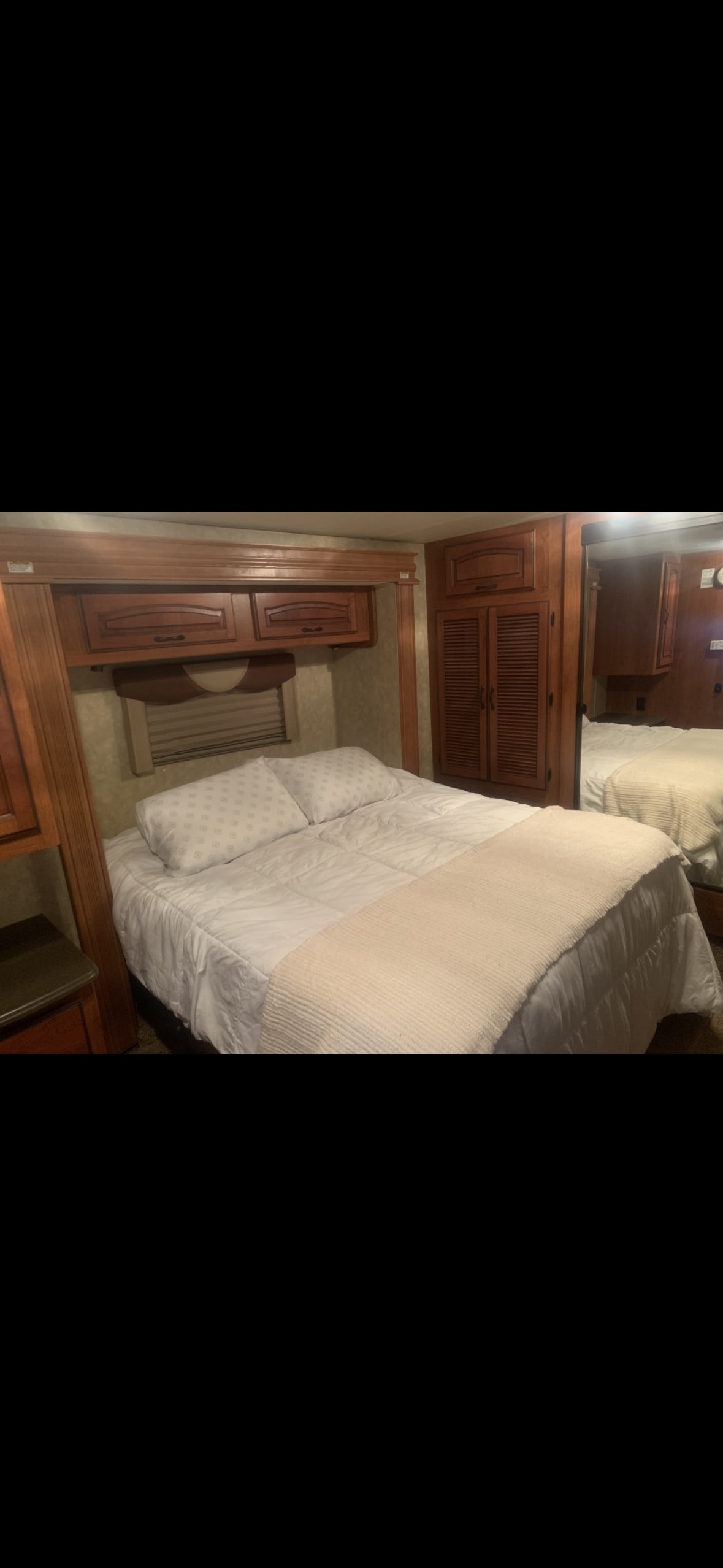 Comfy RV rental bedroom featuring a bed with white bedding, wooden cabinets, a closet, and a full-length mirror.. Coachmen Sportscoach 2011