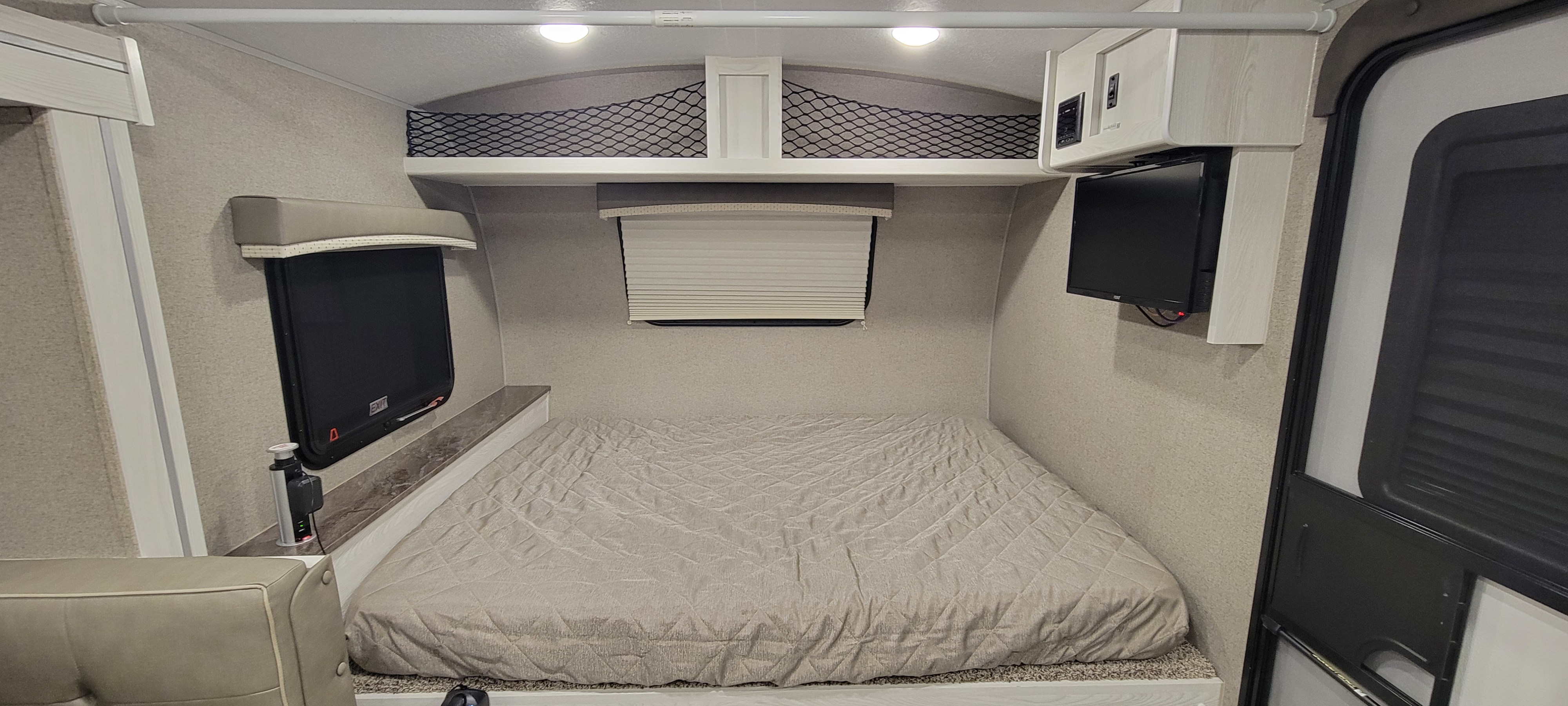 Cozy RV rental bedroom with a quilted bed, windows, mounted TV, pop-up outlet, and overhead storage.. Forest River Rockwood Geo Pro 2020