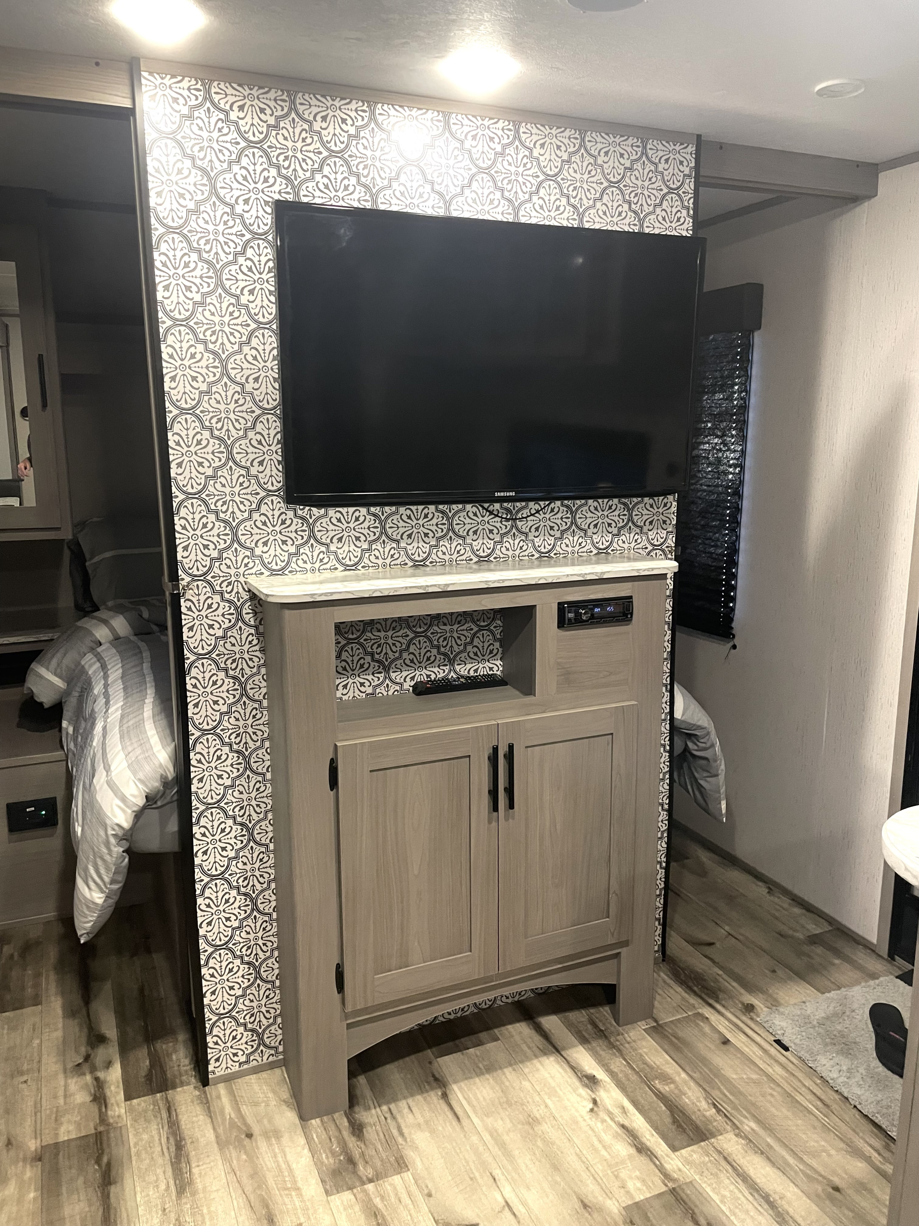 Modern RV rental interior: Wall-mounted TV, media cabinet with patterned wall, and a cozy bed in the sleeping area.. Dutchmen Coleman Lantern LT 2023