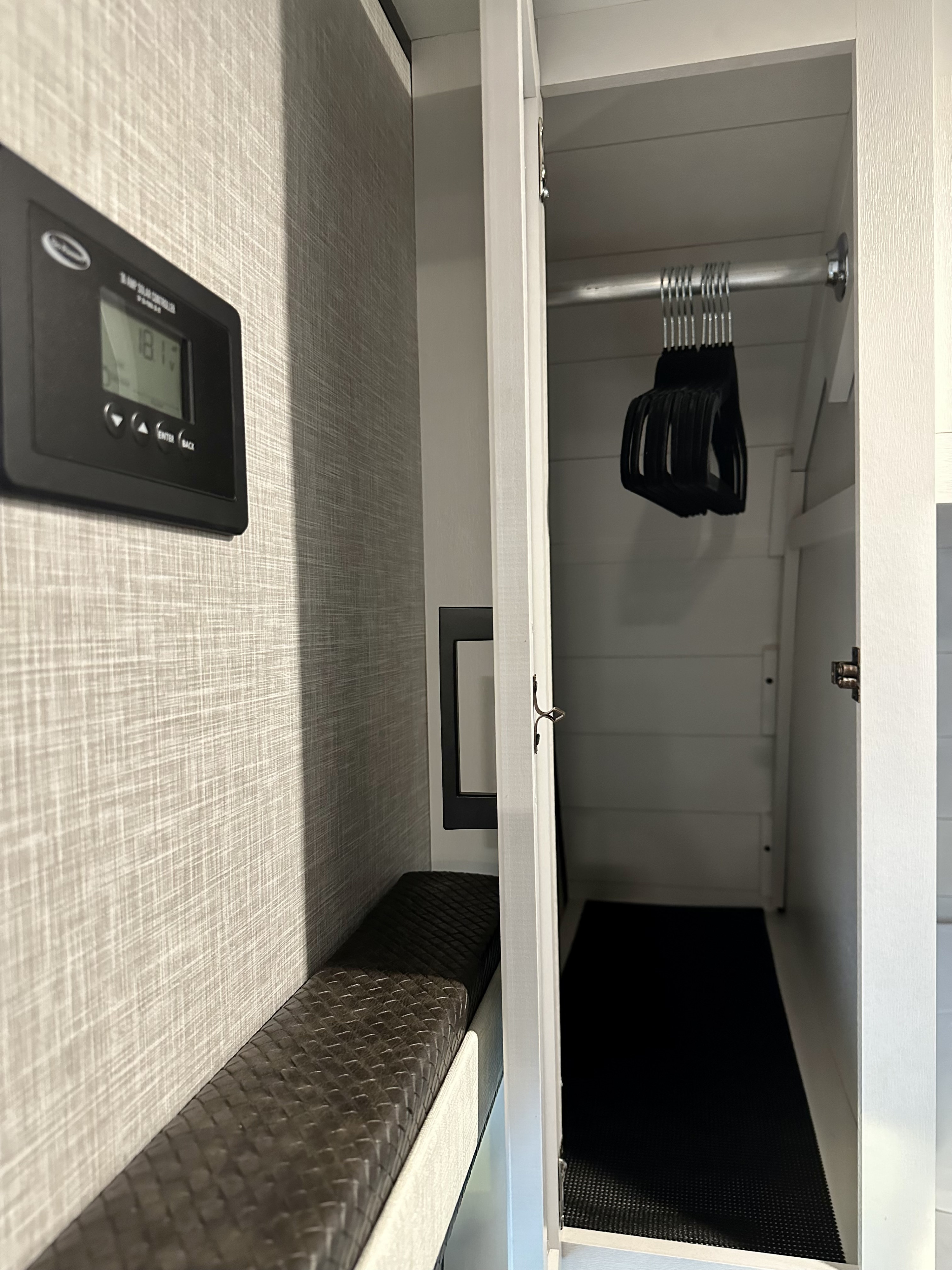 RV rental interior: A compact closet with hangers, a dark bench, and a solar control panel on a textured wall.. Jayco Jay Flight 2024