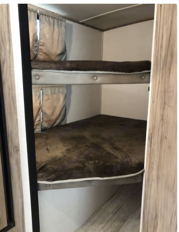 RV rental interior with two cozy bunk beds, brown bedding, and privacy curtains. A compact sleeping area.. Palomino Solaire Ultra Lite 2018