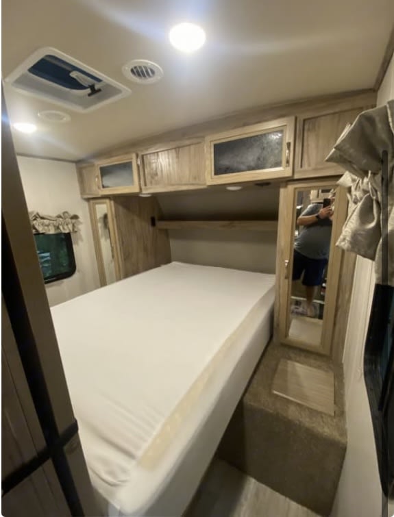 Spacious RV rental bedroom with a white bed, overhead wood-grain cabinets, and a built-in nightstand with a mirror.. Palomino Solaire Ultra Lite 2018
