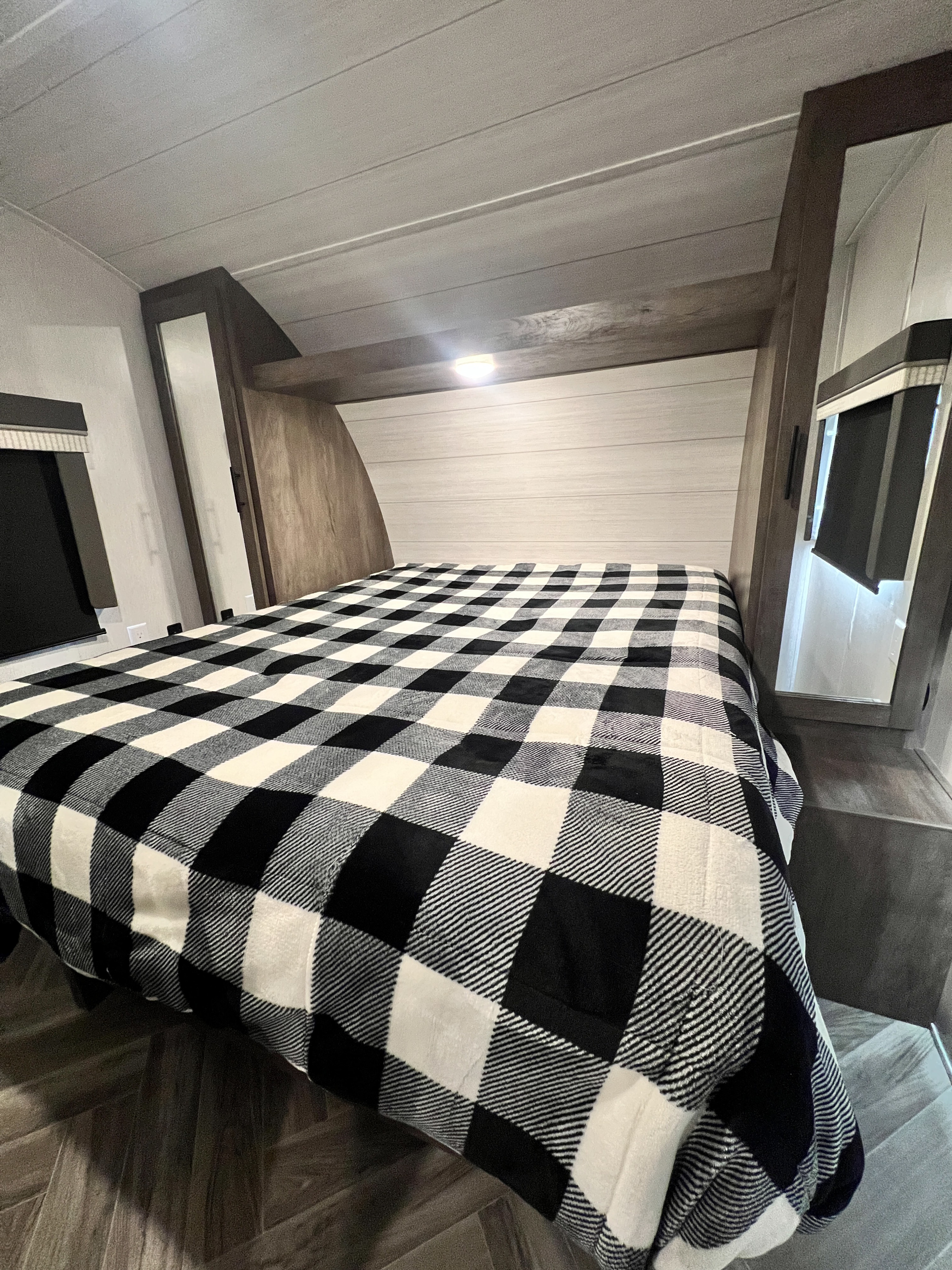 This cozy RV rental bedroom features a bed with a black and white plaid blanket and integrated storage units.. Forest River Salem Cruise Lite 2022