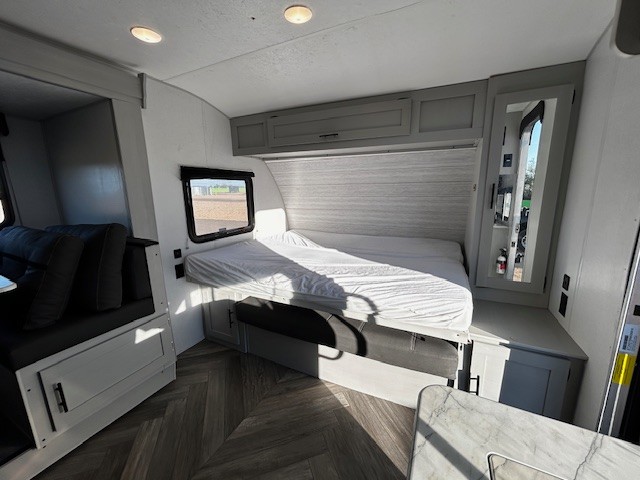 Bright RV rental interior showcasing a cozy bed, dinette, and kitchen, ideal for road trips. Overhead cabinets & mirrored wardrobe visible.. Forest River Wildwood 2021
