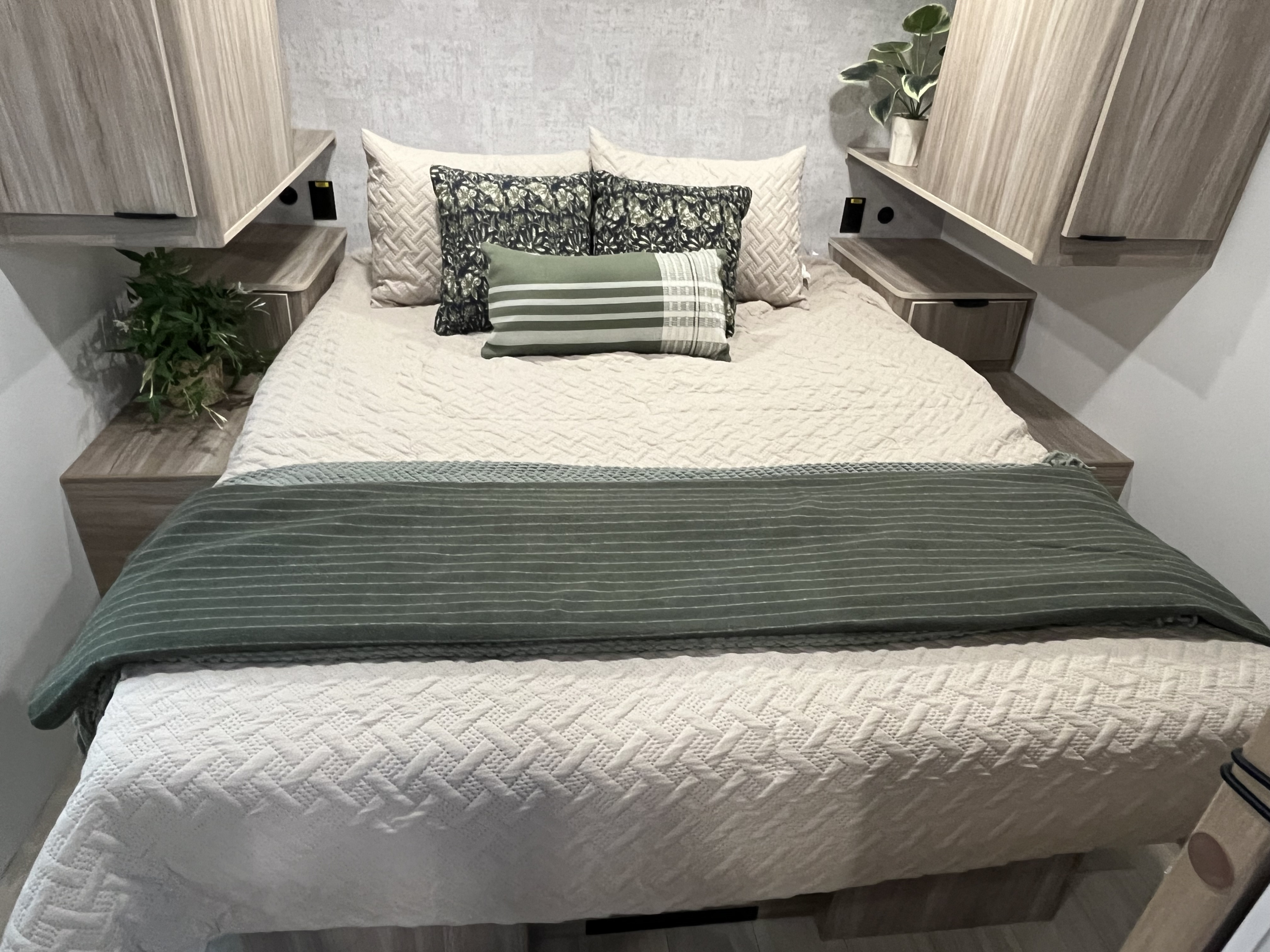 Cozy RV rental bedroom featuring a comfy bed with green & cream bedding, patterned pillows, and modern wood cabinets.. Winnebago Access 26 RL 2024