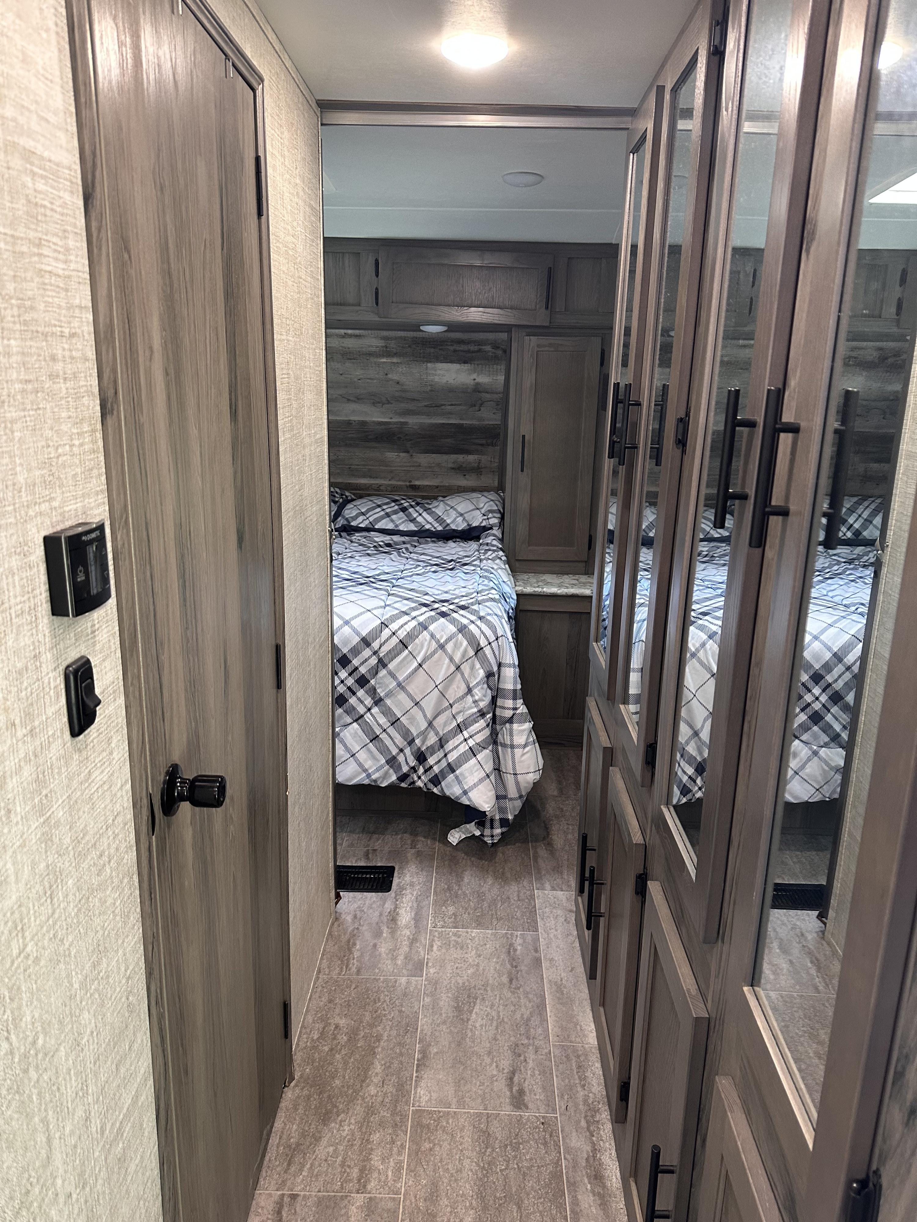 Explore this cozy RV rental's bedroom area, featuring a plaid bed, mirrored closets, and wood-grain interior.. Gulf Stream Conquest 2020