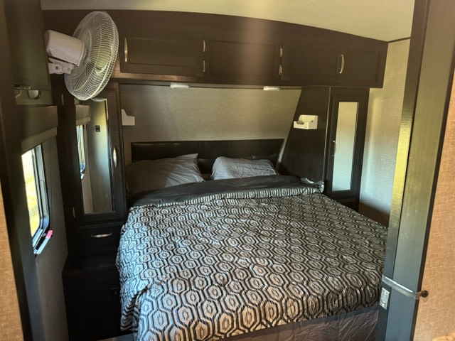 Cozy RV rental bedroom featuring a queen bed with overhead storage, side closets, and a mounted fan. Perfect for travel adventures.. Grand Design RVM-178 / Imagine 2018
