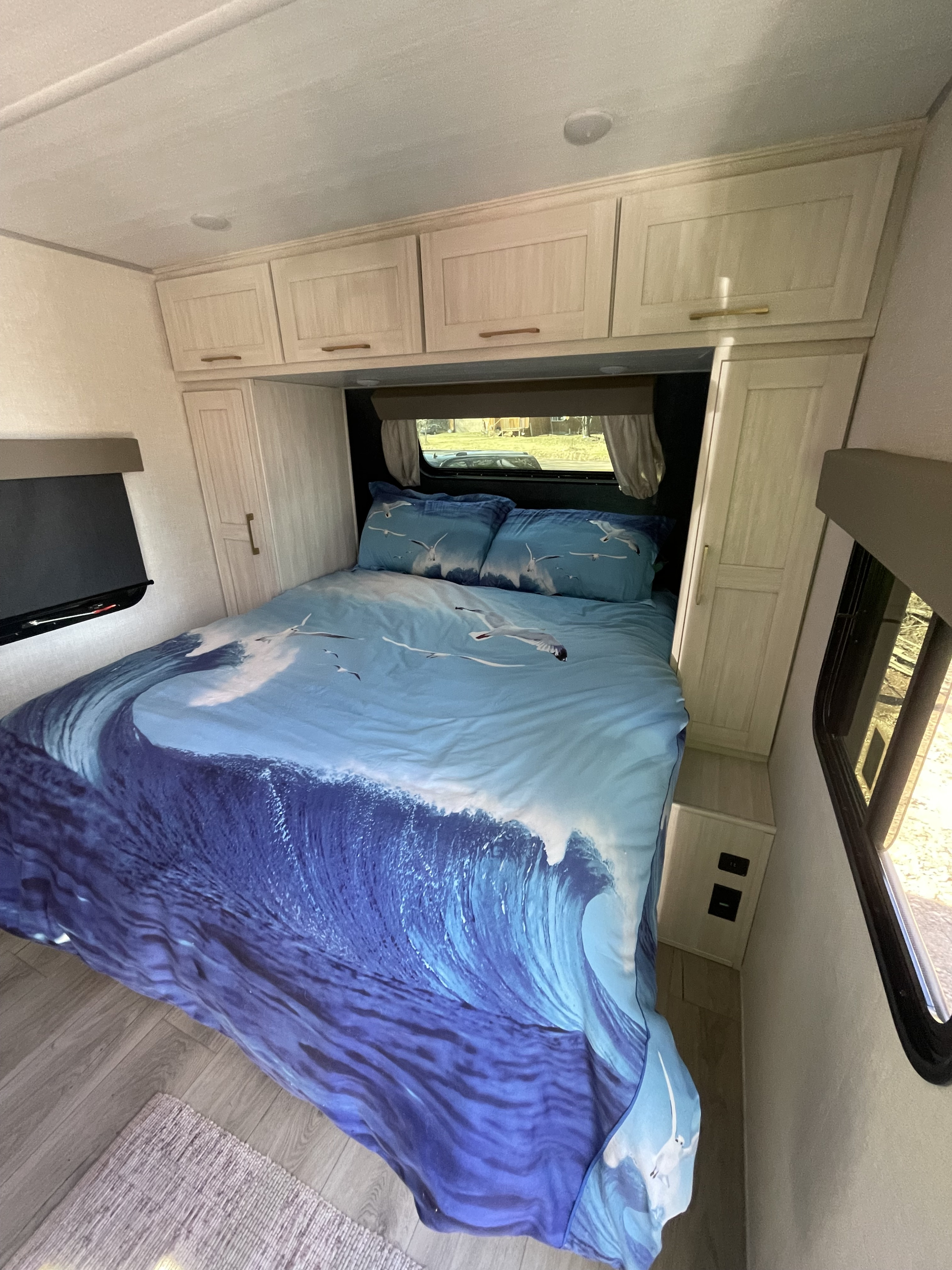 Cozy RV rental bedroom with wave-themed bedding, overhead cabinets, and a TV for comfortable travel and camping.. Forest River Surveyor Legend 19SSLE 2024