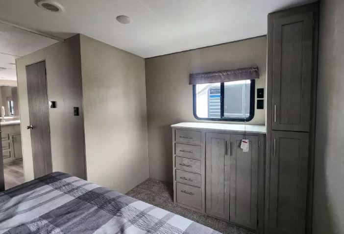 Cozy RV rental bedroom featuring ample storage with dresser and cabinets, plus a window for natural light. Door leads to the bathroom.. Forest River Catalina 2022