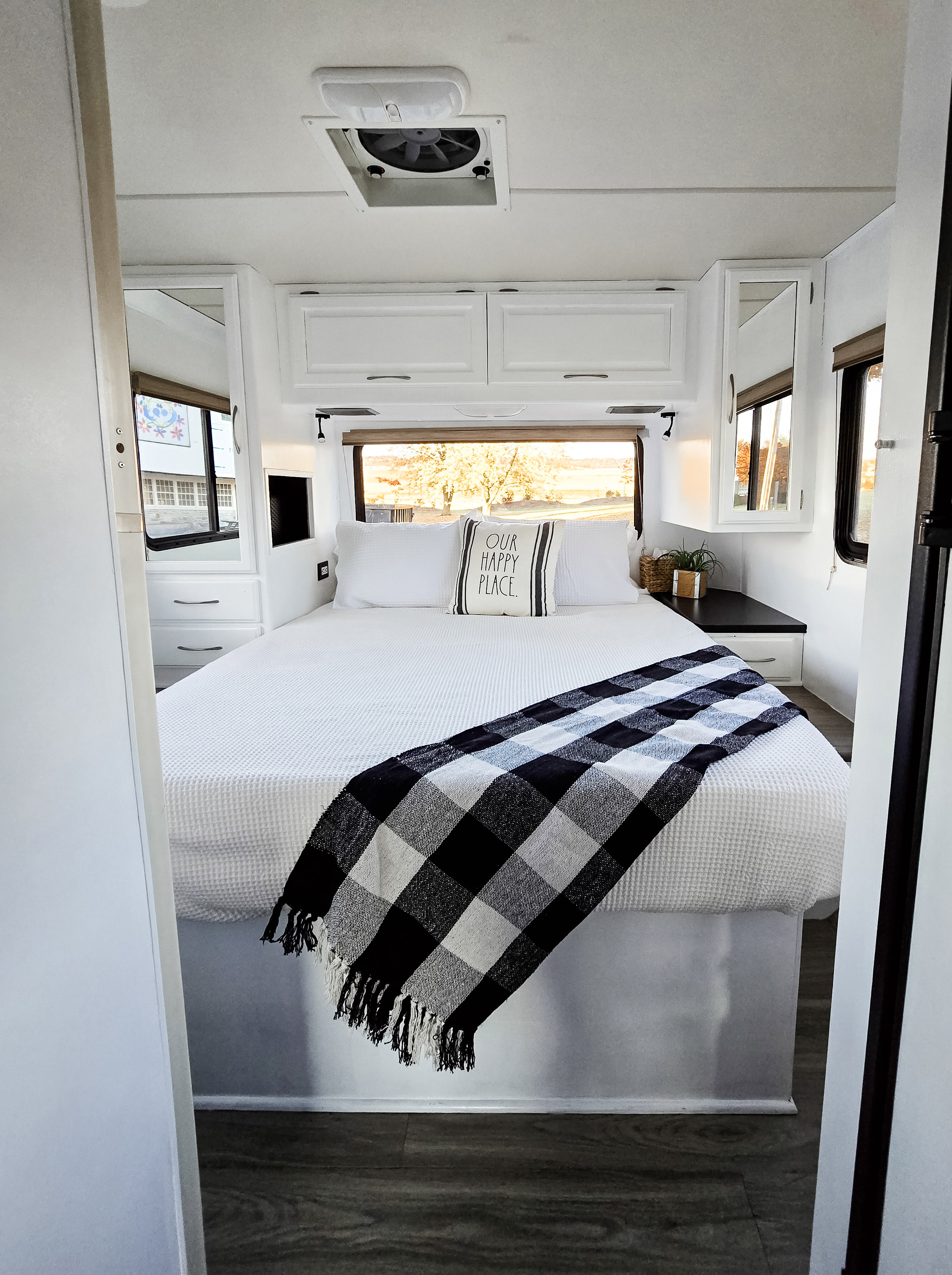Cozy, modern white RV rental bedroom featuring a queen bed with black and white accents, "OUR HAPPY PLACE" pillow, and bright window view.. Four Winds Chateau 2011