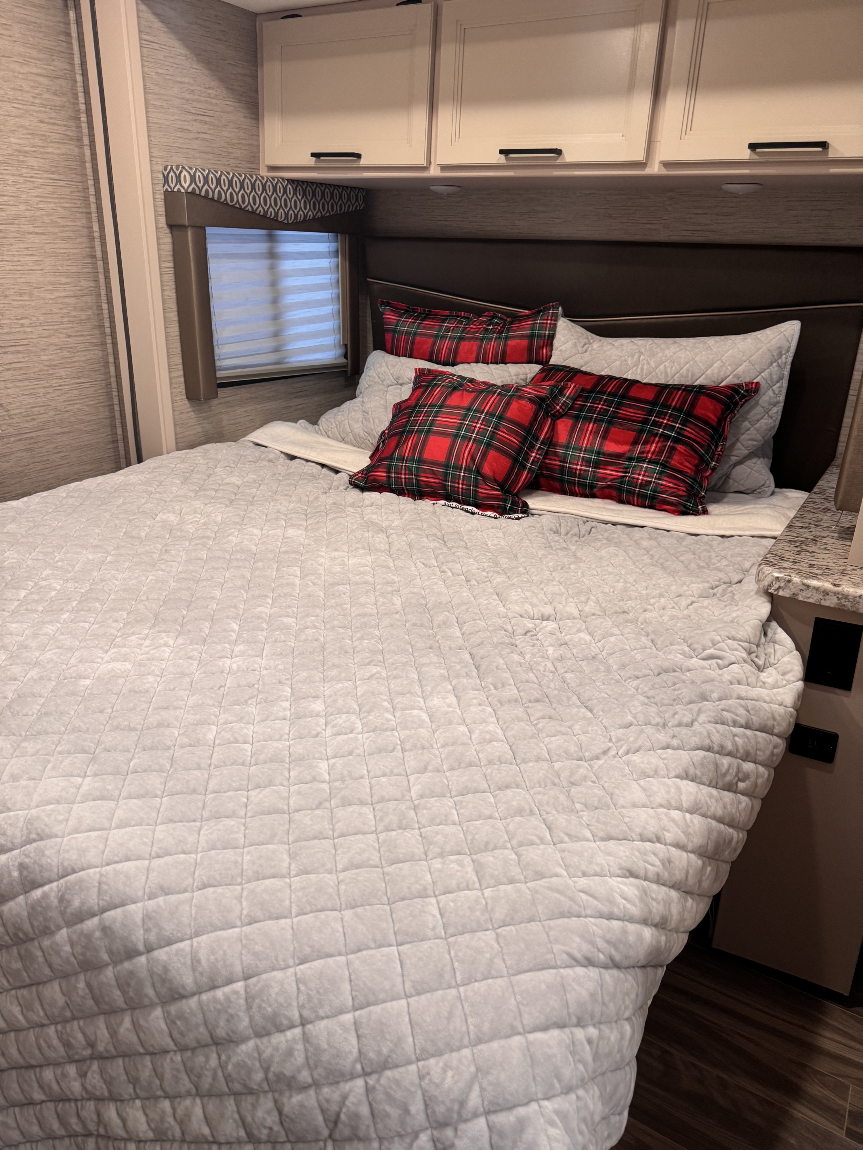 Comfortable RV rental bedroom featuring a cozy quilted bed, plaid pillows, and overhead cabinets.. Thor Freedom Elite 2022