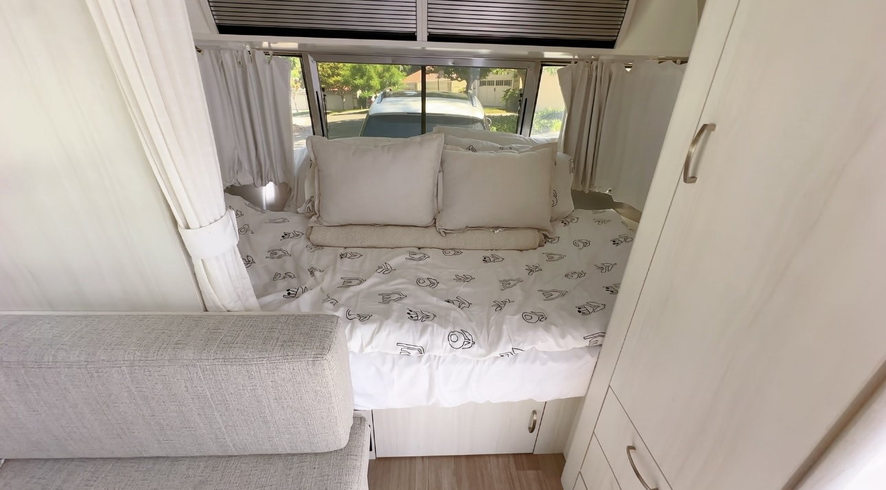 Spacious RV rental interior featuring a bright bed with patterned duvet, pillows, window view, and built-in storage.. Airstream Bambi 2022