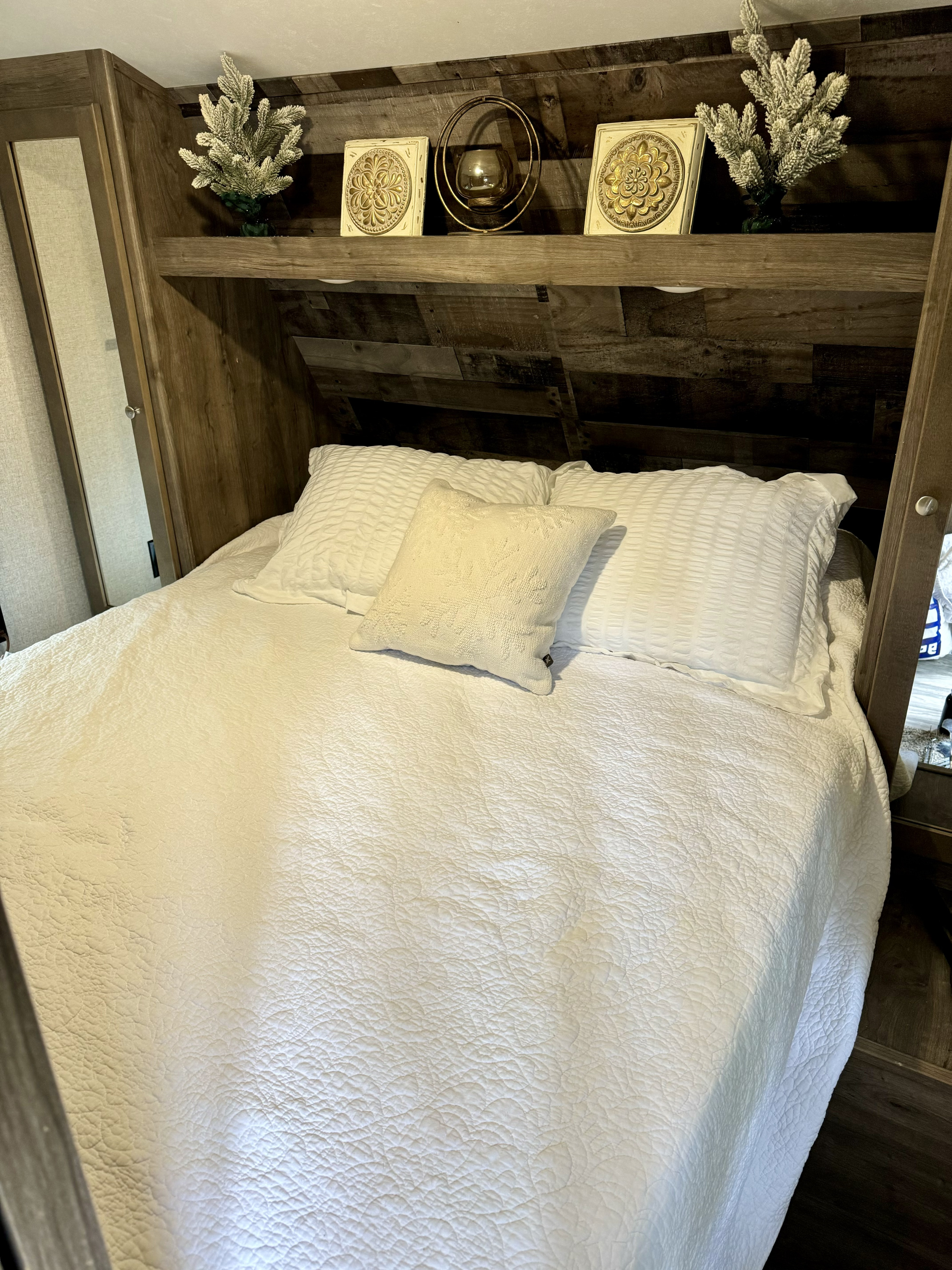 This comfy RV rental bedroom showcases a bright white bed, quilted spread, and decorative overhead shelf with nature-themed decor.. Aspen Trail Aspen Trail Trailer 2019