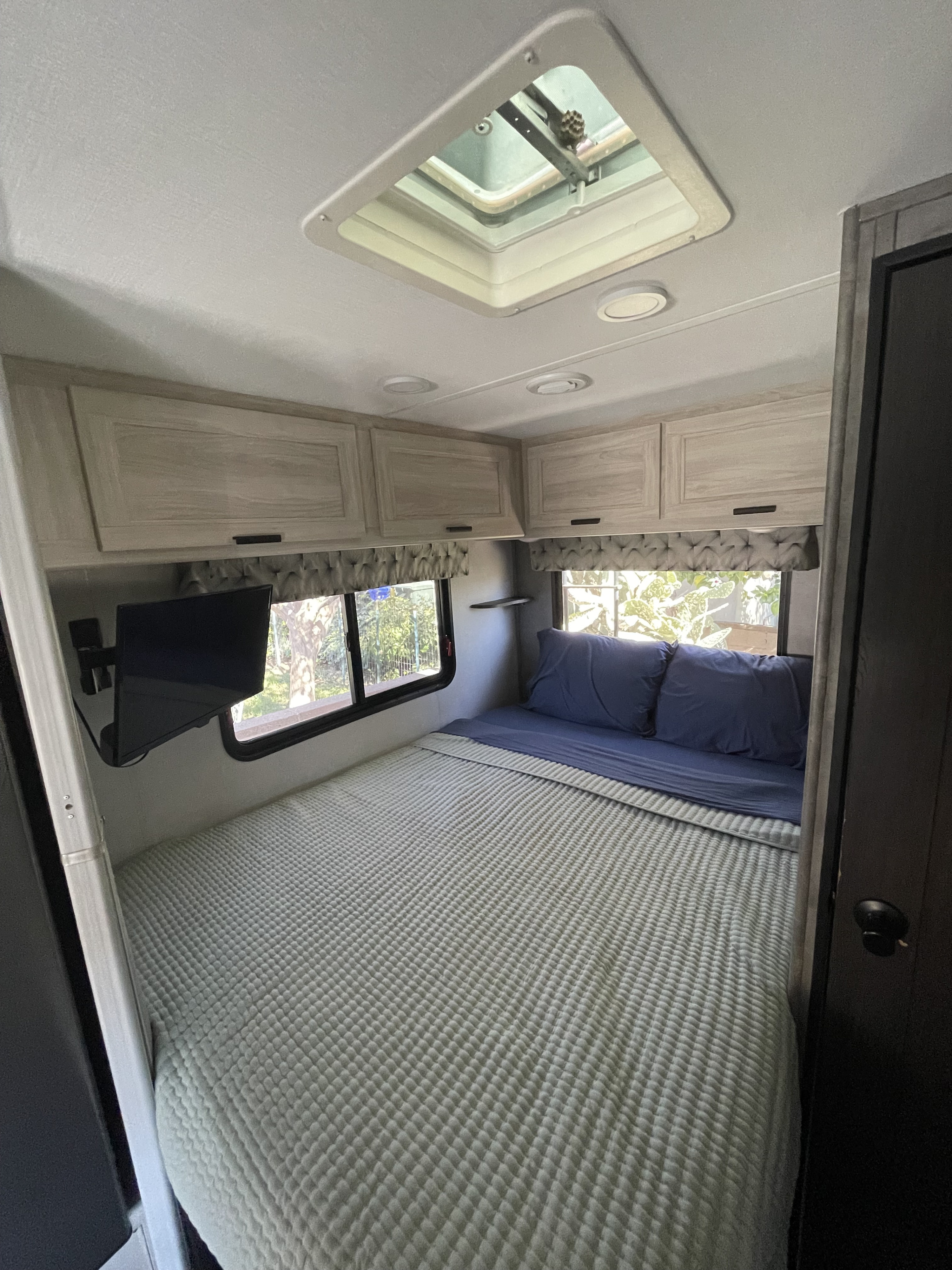 A comfortable RV rental bedroom with a bed, wall-mounted TV, overhead cabinets, and a ceiling vent.. Forest River Sunseeker LE 2022