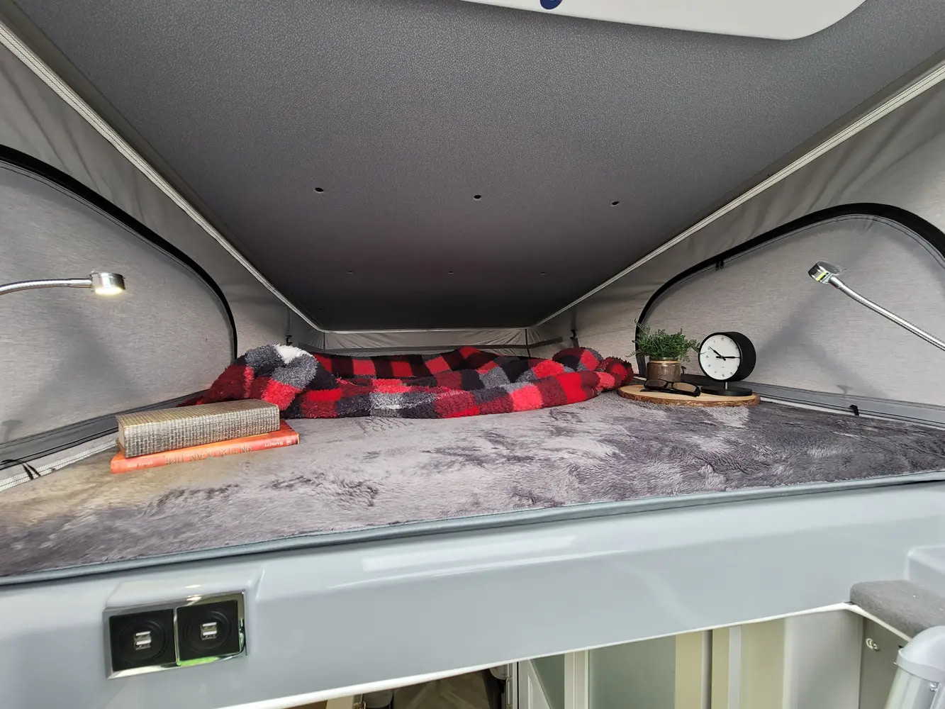 An RV rental's cozy pop-top bed with soft blankets, reading lights, books, and convenient USB charging ports.. Forest River Coachmen Nova 2026