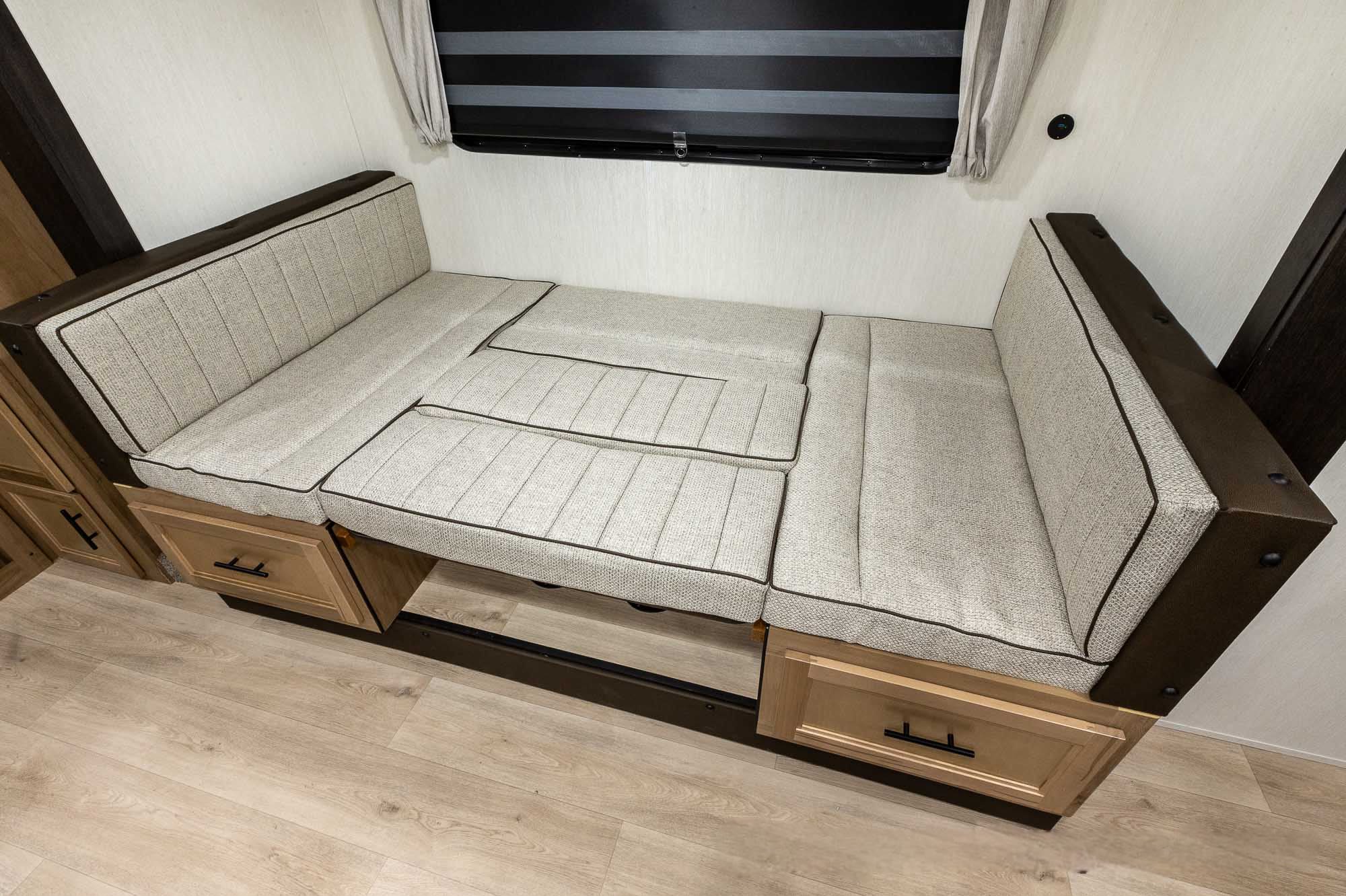 Bright RV rental interior showing a versatile dinette with light cushions, dark trim, and storage drawers, converting to a bed.. Forest River 23dbh 2025