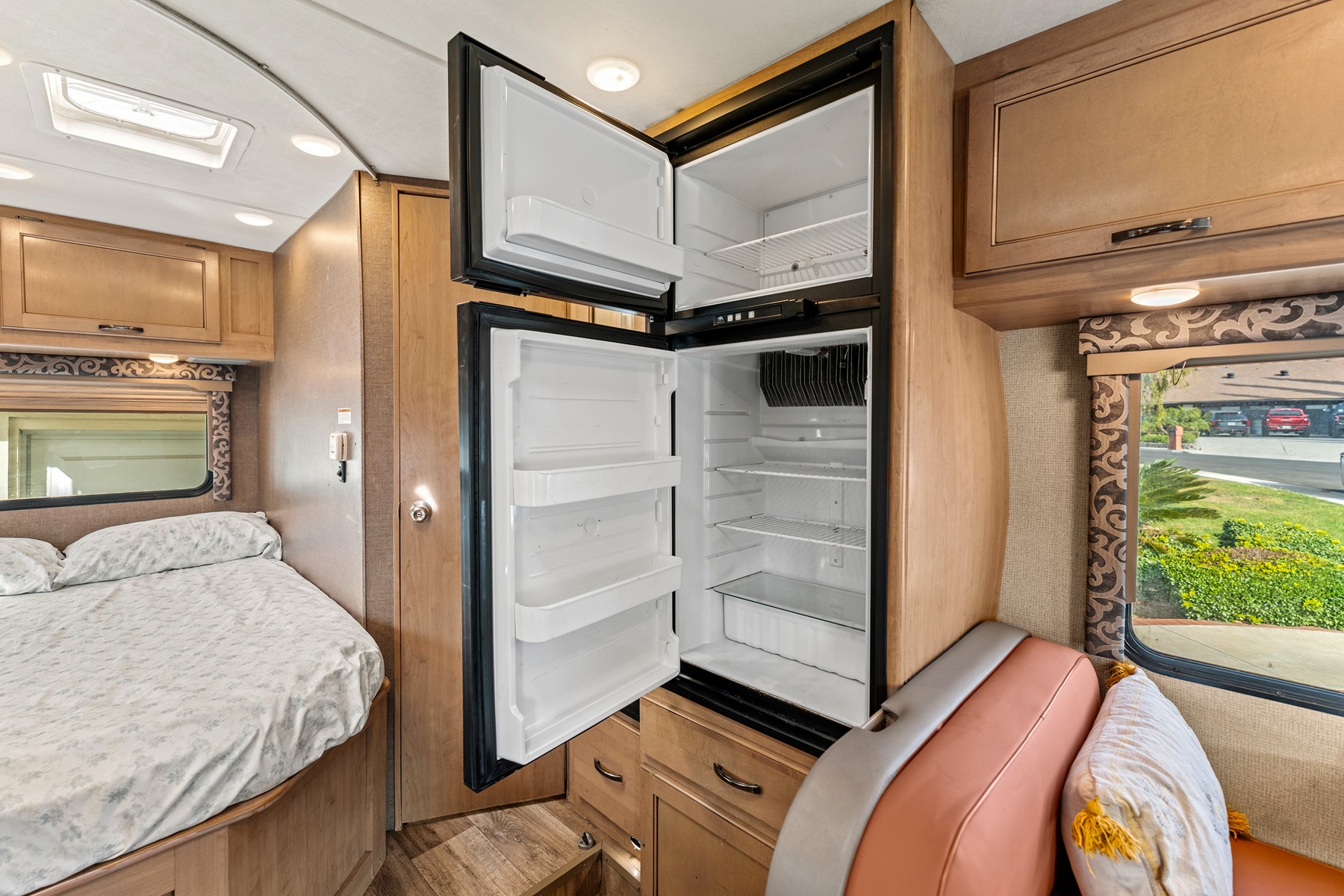 Inside this RV rental: a cozy bed, open two-door refrigerator, and wooden cabinetry, ready for your adventure.. Thor Four Winds 2019