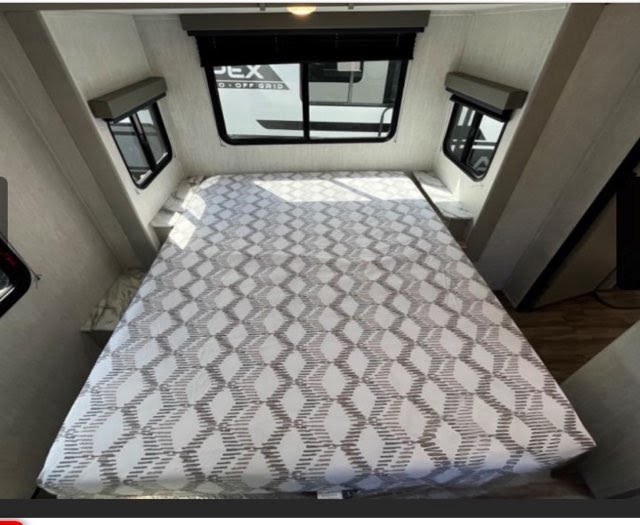 Spacious RV rental bedroom with a large bed, multiple windows, and built-in shelving, perfect for a comfortable trip.. Coachmen Apex 2024