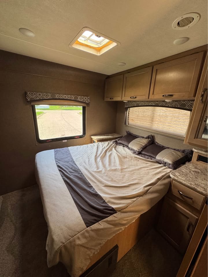 Cozy RV rental bedroom featuring a bed, window with outdoor view, overhead cabinets, and ceiling skylight.. Thor Motor Coach Chateau 2019