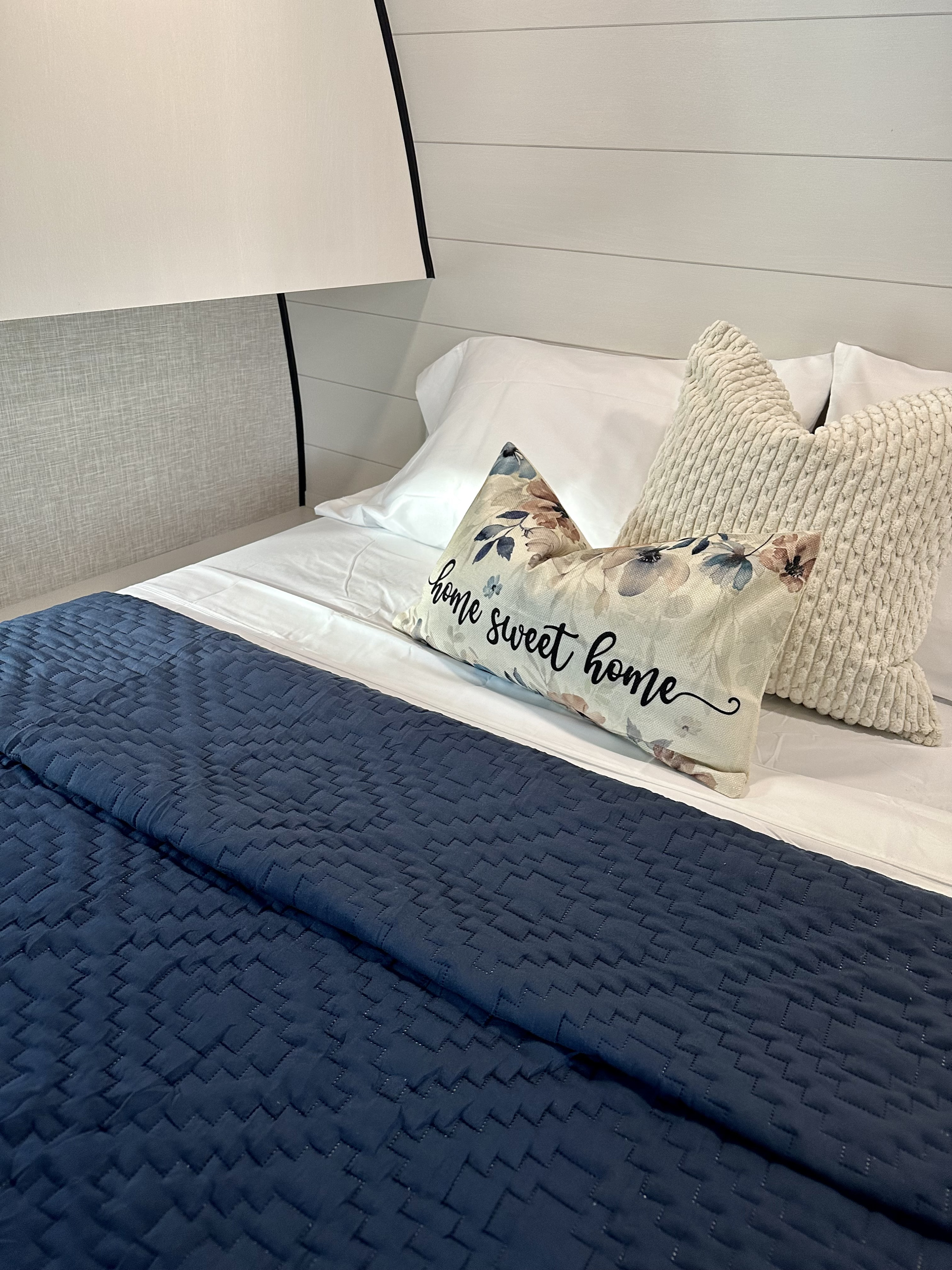 Inside your RV rental: A comfy bed with crisp white sheets, a dark blue quilt, and a 'home sweet home' pillow.. Jayco Jay Flight 2024