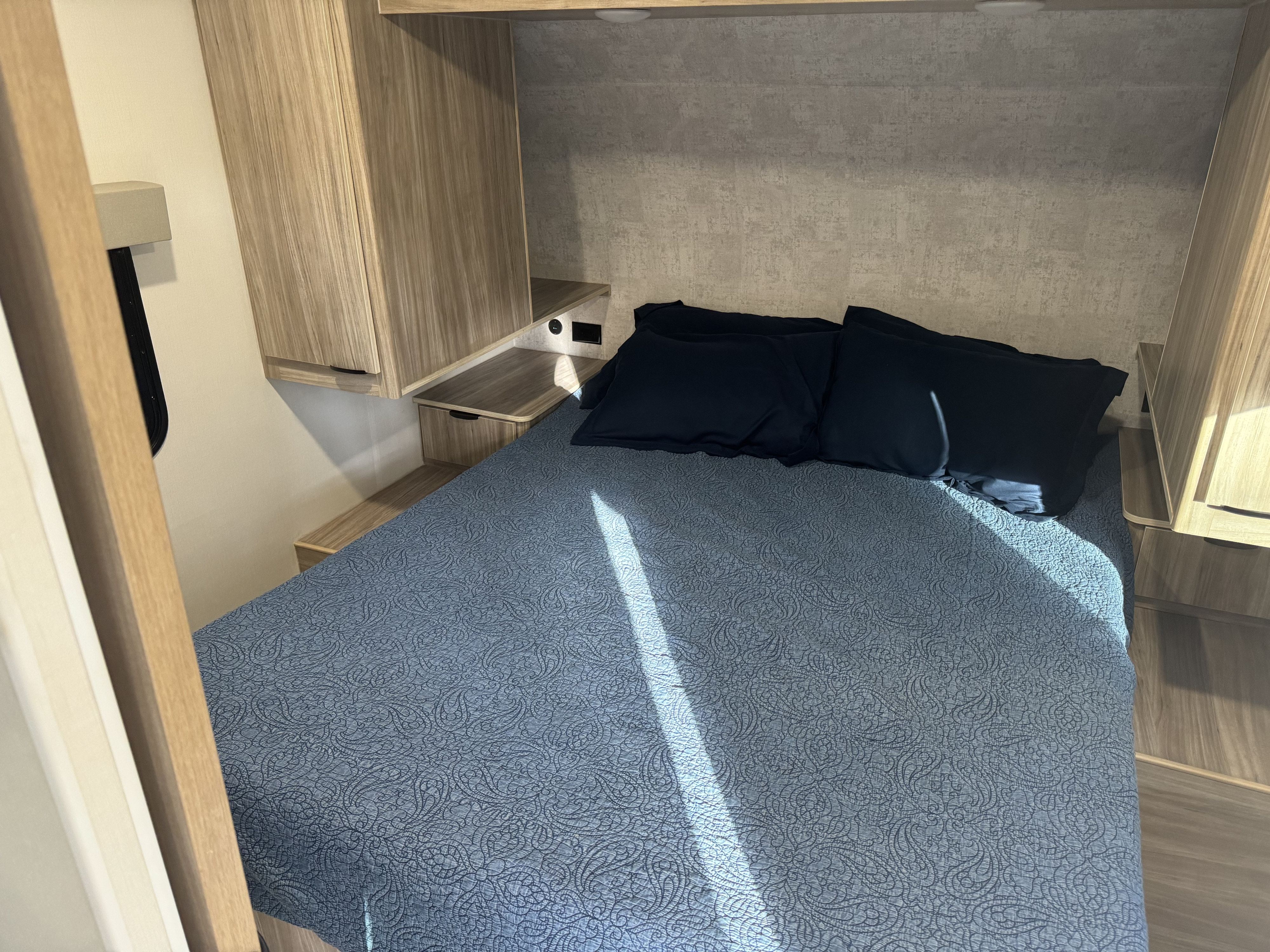 Comfortable RV rental bedroom with built-in storage, a patterned bedspread, and dark pillows.. Winnebago Access 2024
