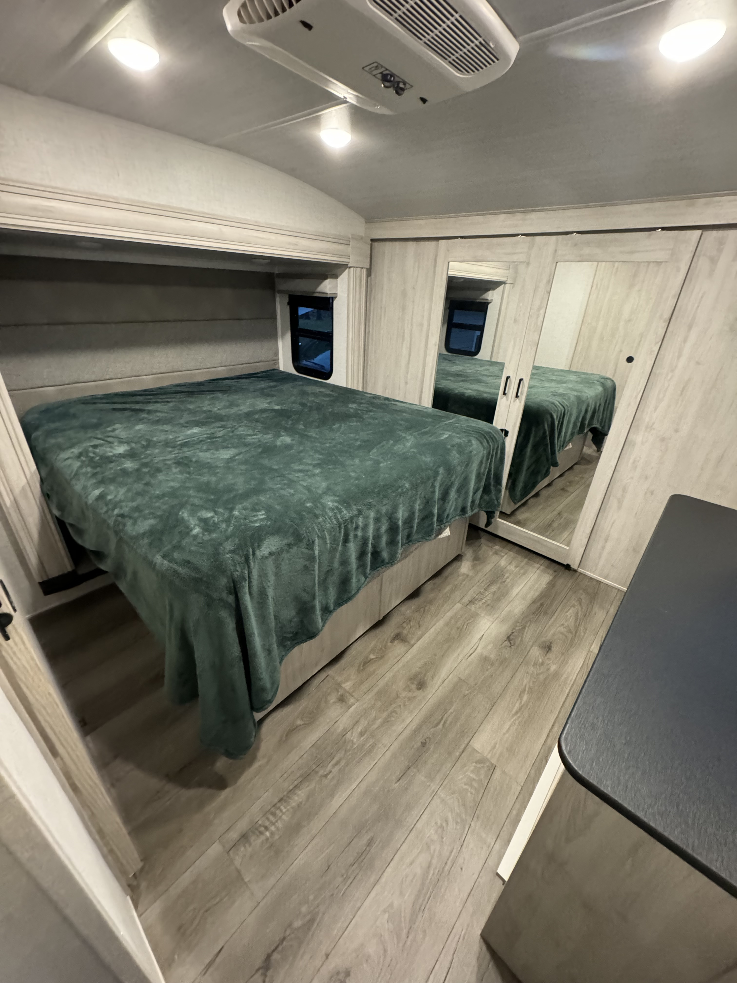 Spacious modern RV rental bedroom featuring a bed with green blanket, mirrored closet doors, and light wood-look flooring.. East to West Tandara 2022