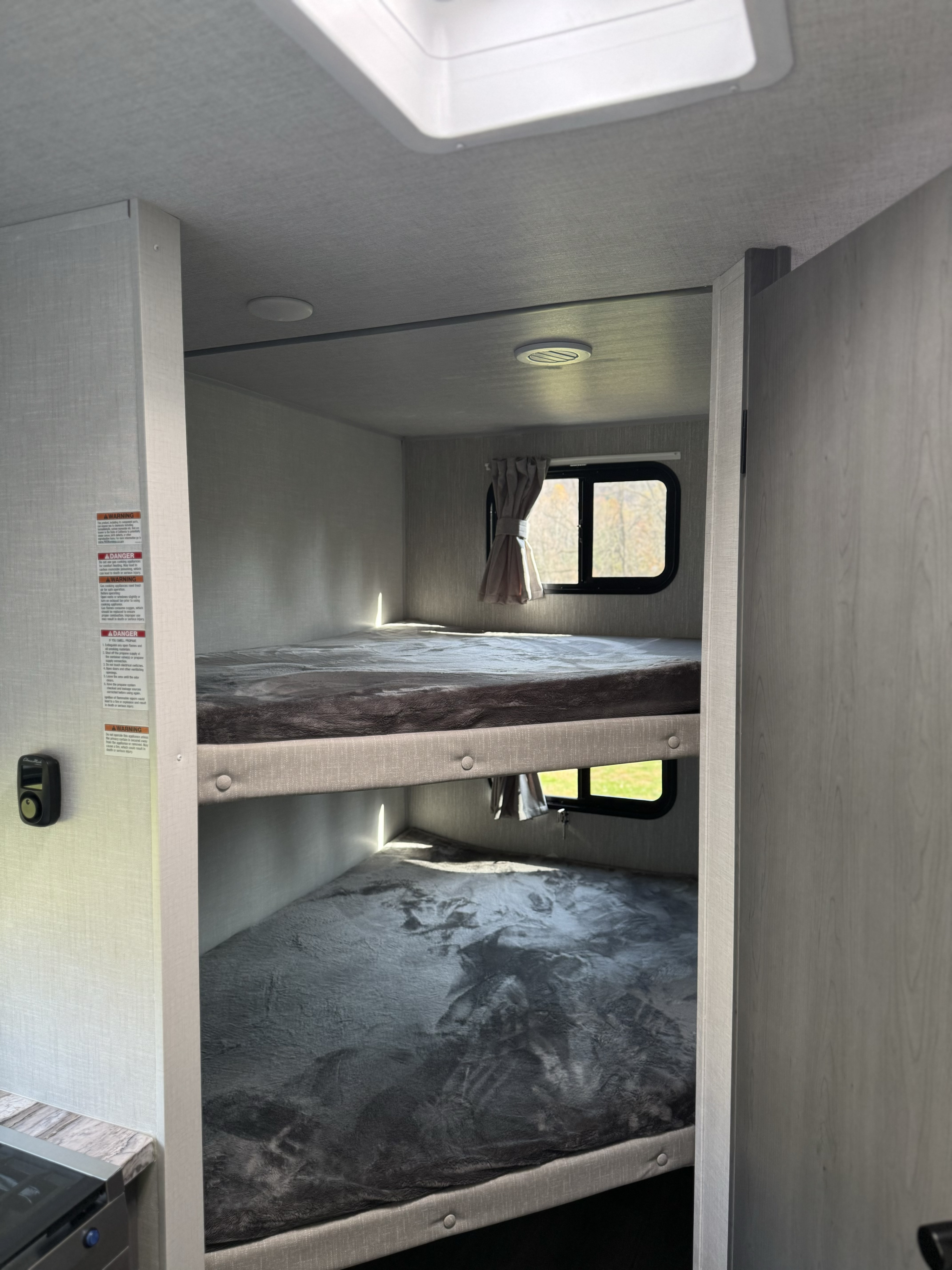 Cozy bunk beds inside an RV rental, complete with soft grey bedding, small windows, and warm natural light.. Forest River Ozark 2025