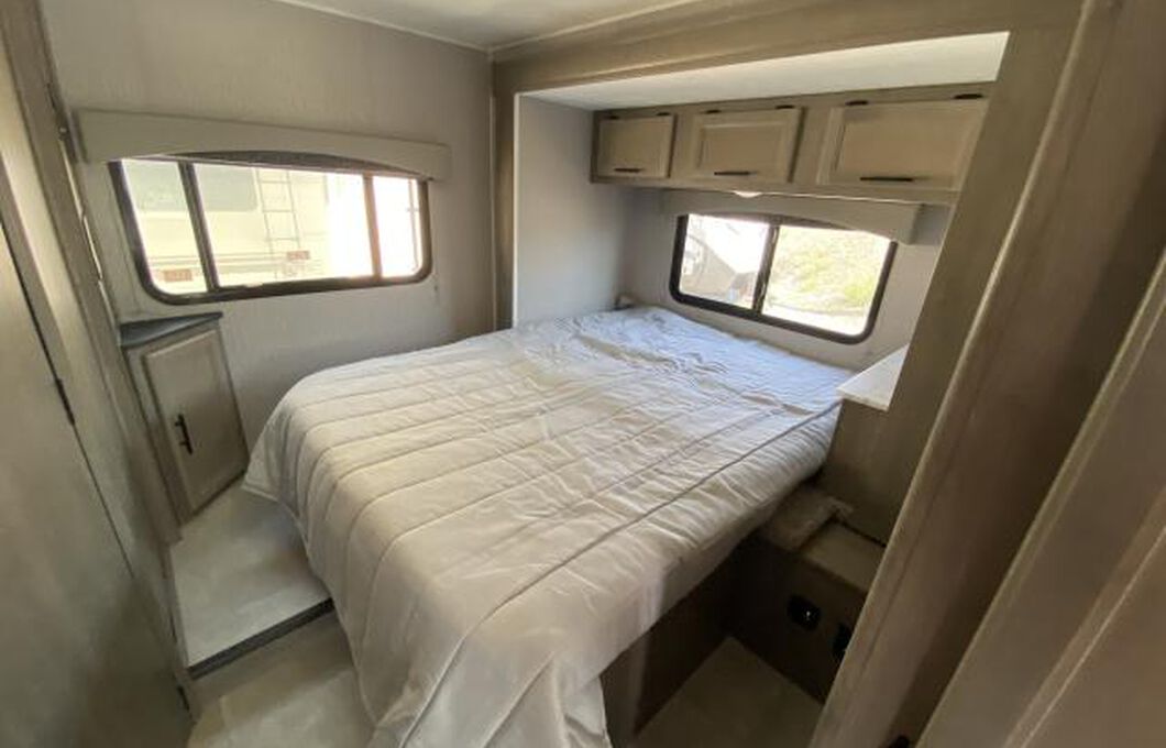 Cozy RV rental bedroom with a comfortable bed, side windows, and overhead storage cabinets.. COACHMEN FREELANDER 21RS 2023