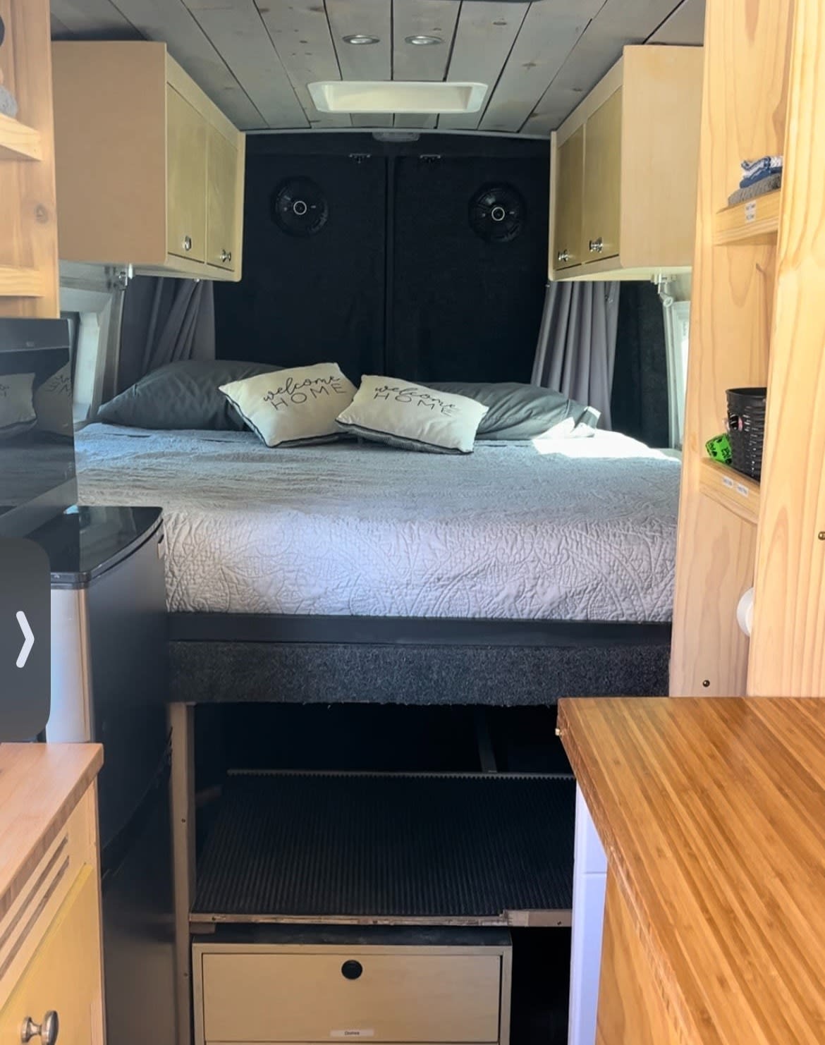 Inside this RV rental, find a cozy camper van interior with bed, overhead cabinets, and clever storage.. Mercedes Sprinter 2020