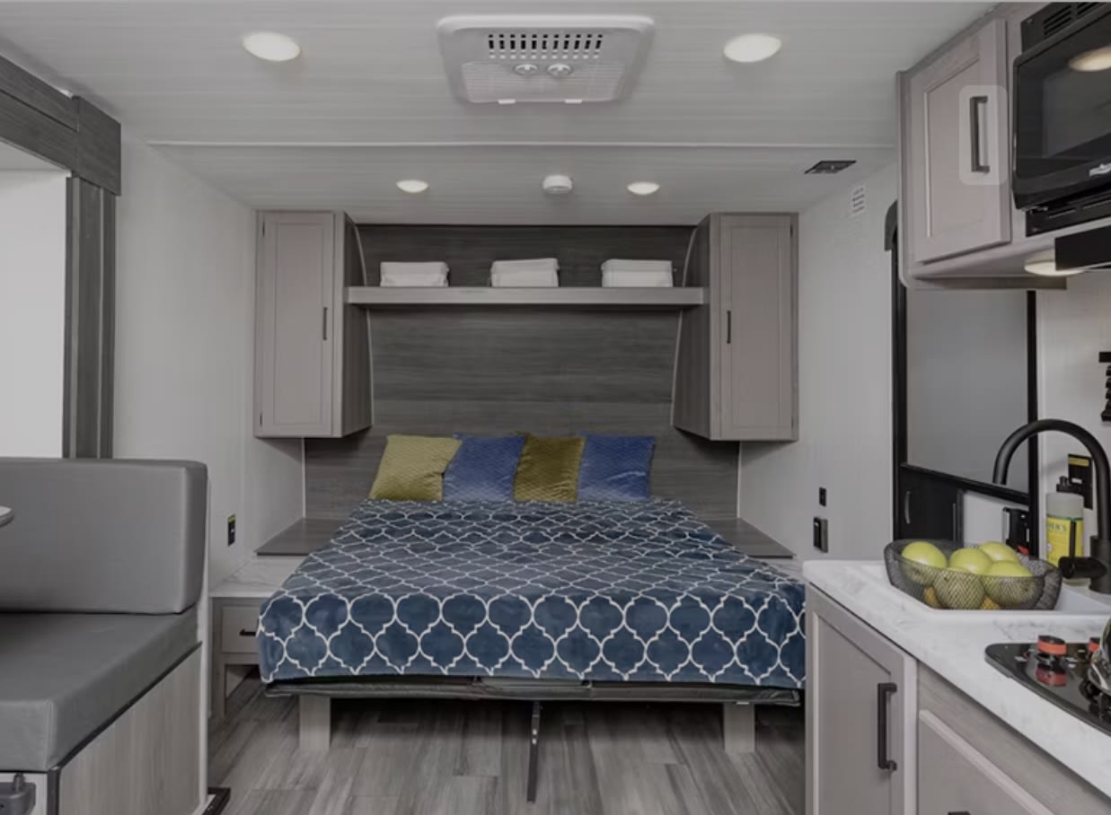 Modern RV rental interior: a comfy bed, overhead storage, kitchen with sink, and dinette. Ideal for travel & camping.. Keystone RV Hideout Sport 2024