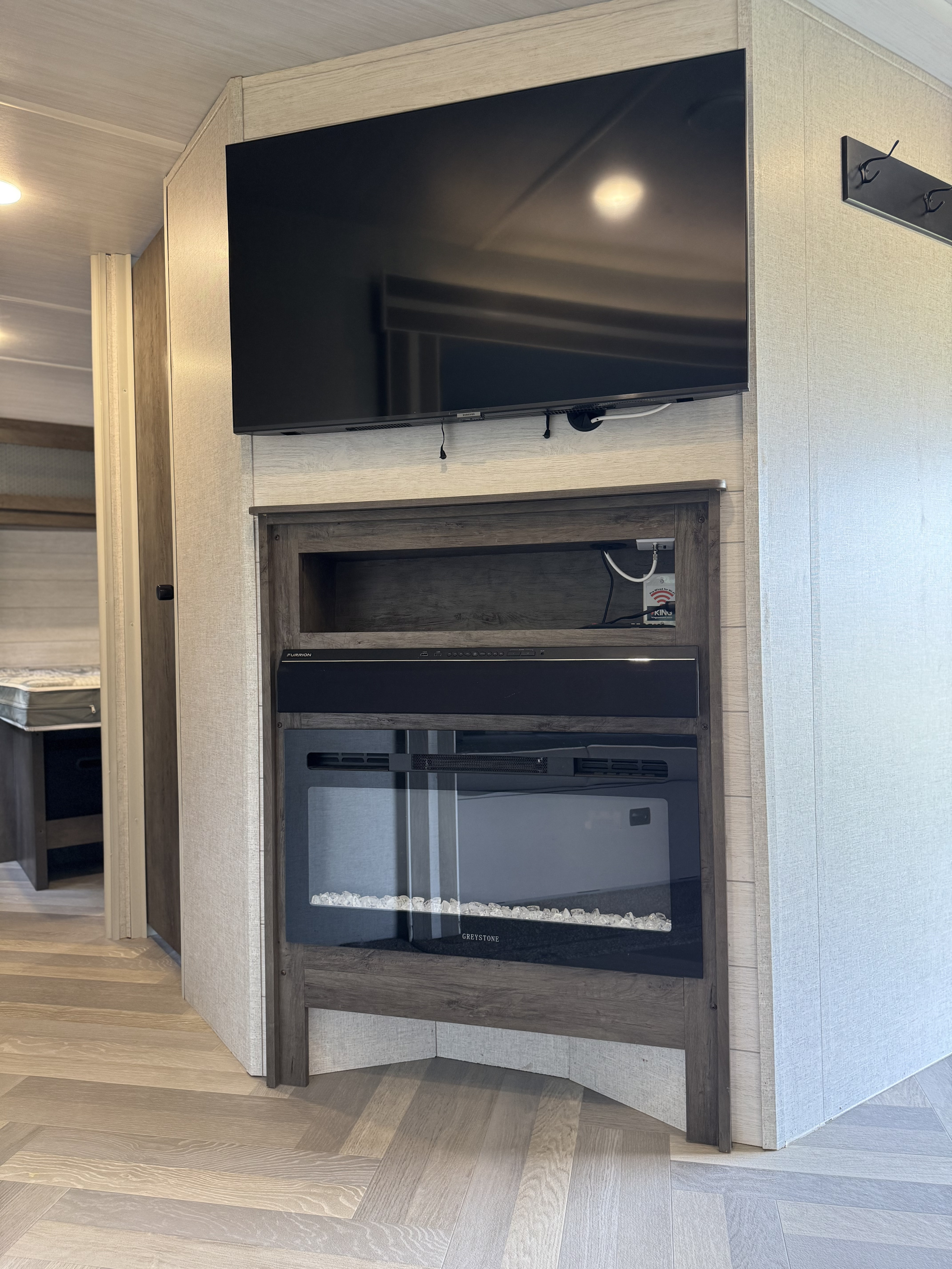 RV rental living space with entertainment center, including TV, Furrion soundbar, and electric fireplace, plus herringbone flooring.. Forest River Wildwood 2021