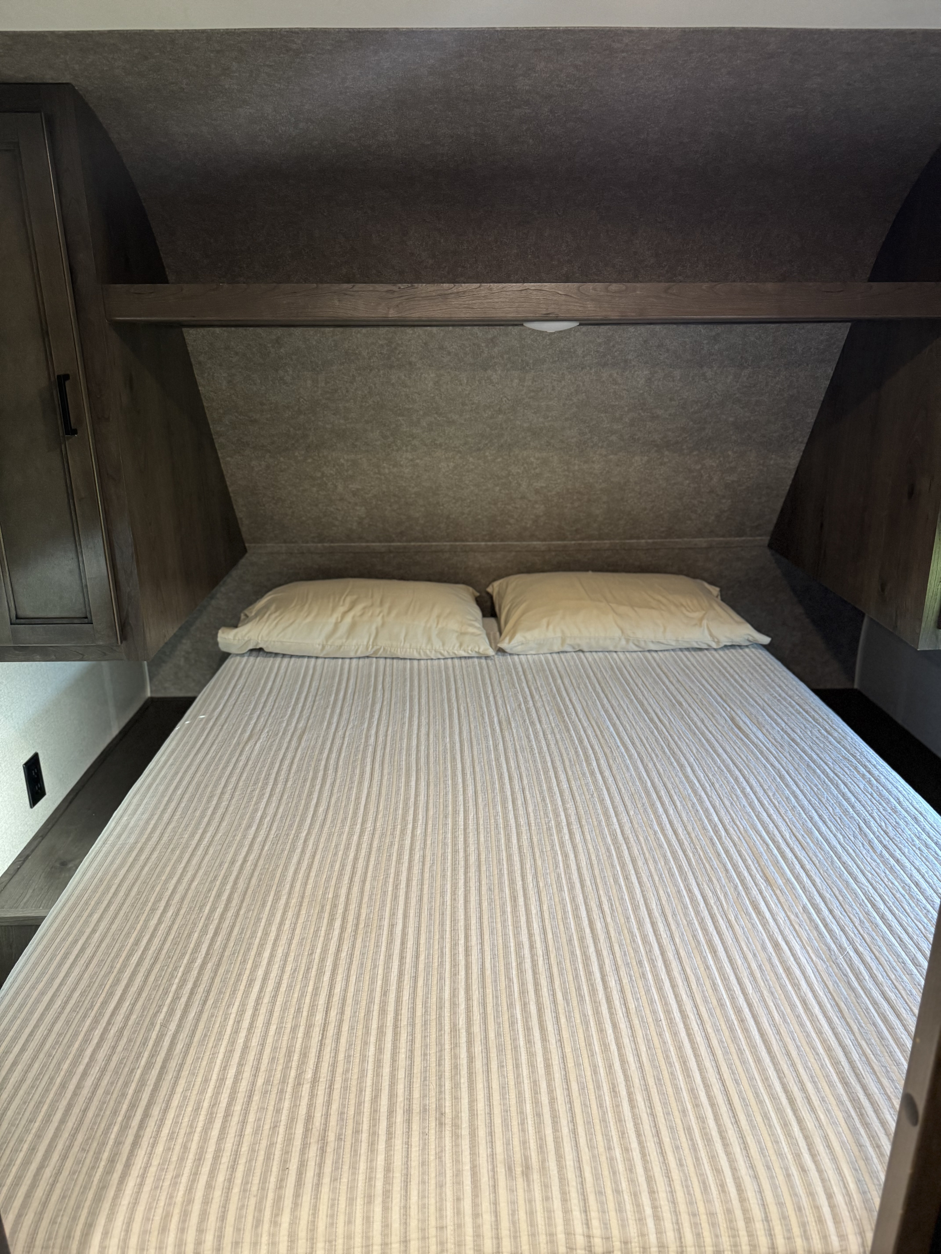 Cozy RV rental bedroom with a striped bedspread, two pillows, and convenient overhead storage.. Starcraft Autumn Ridge 2021