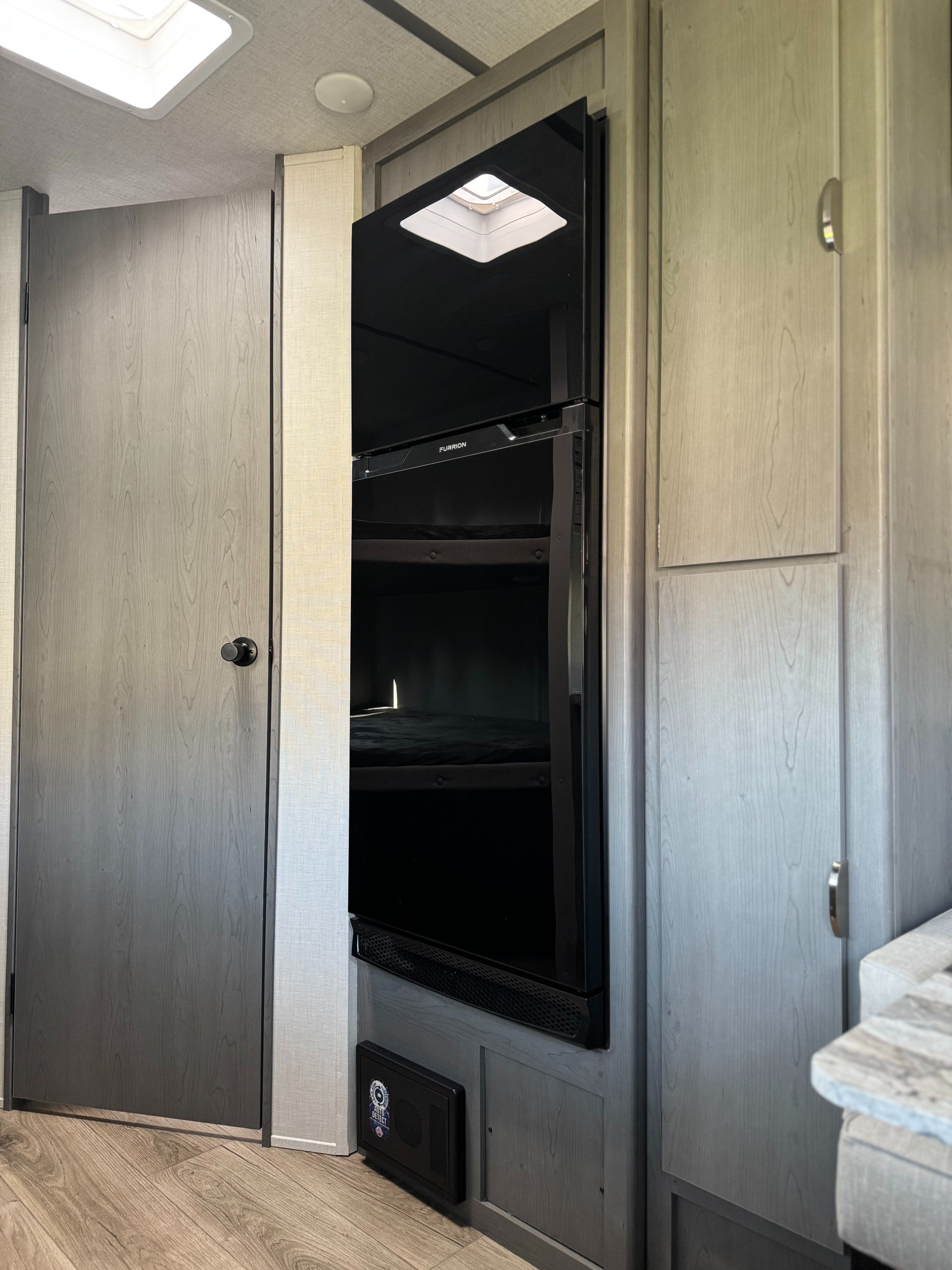Compact RV rental interior features a Furrion refrigerator, wood cabinetry, and a cozy bunk bed. Perfect for travel!. Forest River Ozark 2025