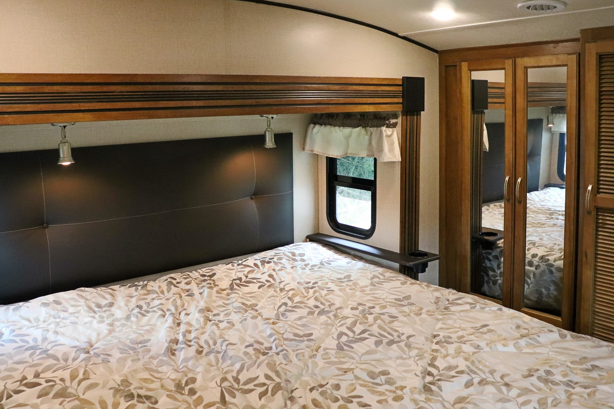 Cozy RV rental bedroom featuring a comfy bed with a patterned comforter, headboard, window, and mirrored storage.. Forest River Coachmen Chaparral 2018