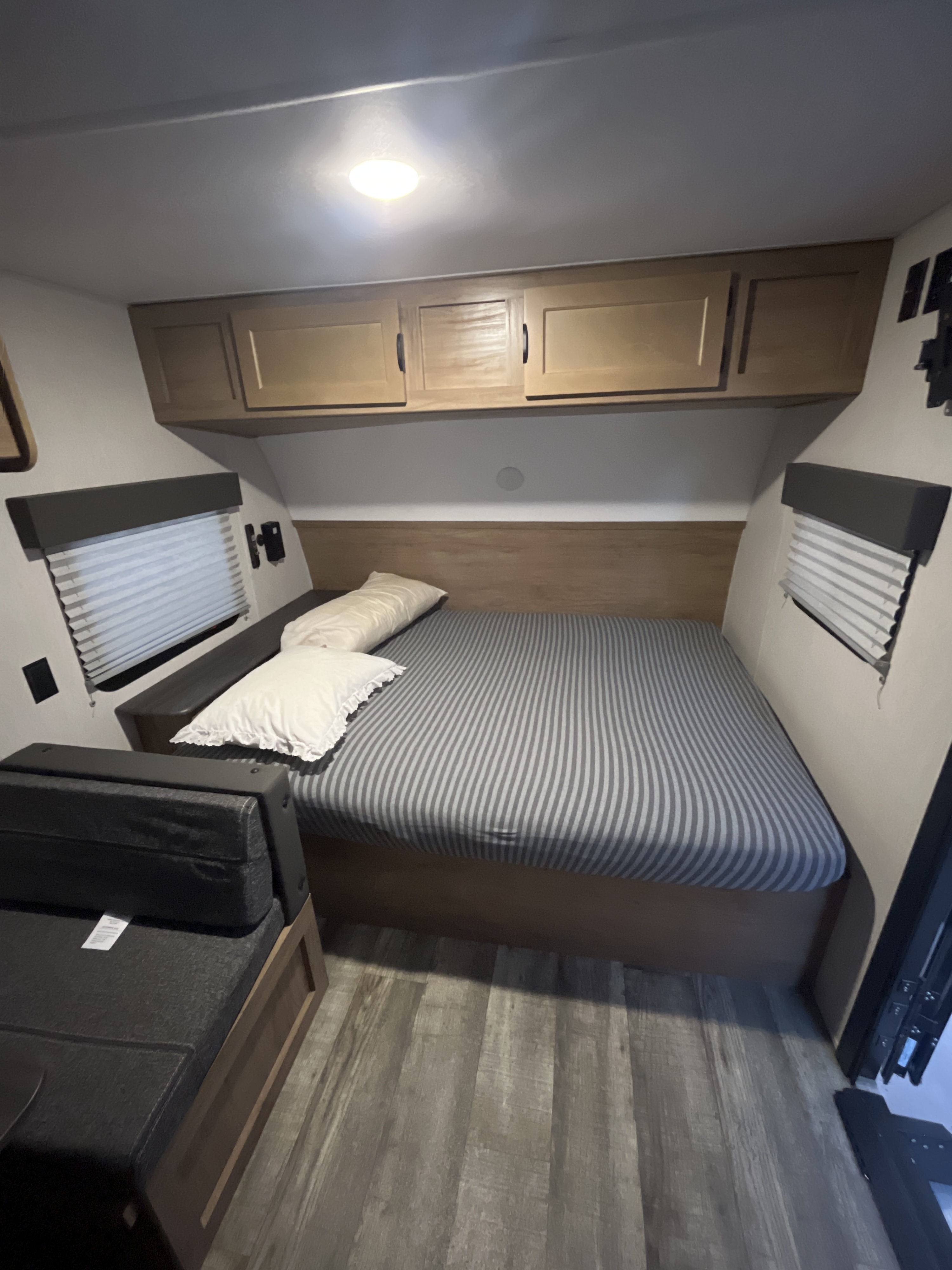 A cozy RV rental bedroom features a bed with striped bedding, overhead cabinets, and wood-look flooring.. Forest River Wolfpup16bhs 2024