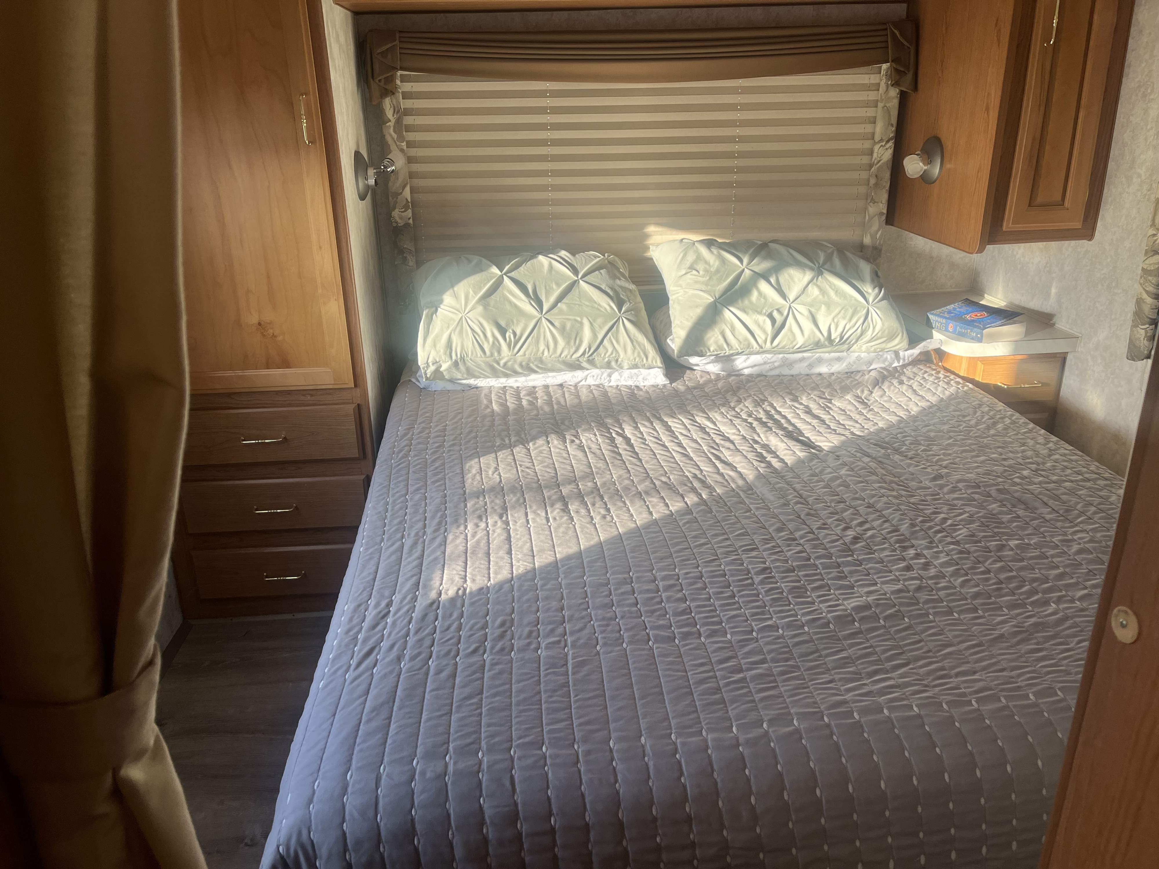 Cozy RV rental bedroom featuring a sunlit bed with light bedding, pillows, and wooden cabinets.. Tioga Tioga Motorhome 2000