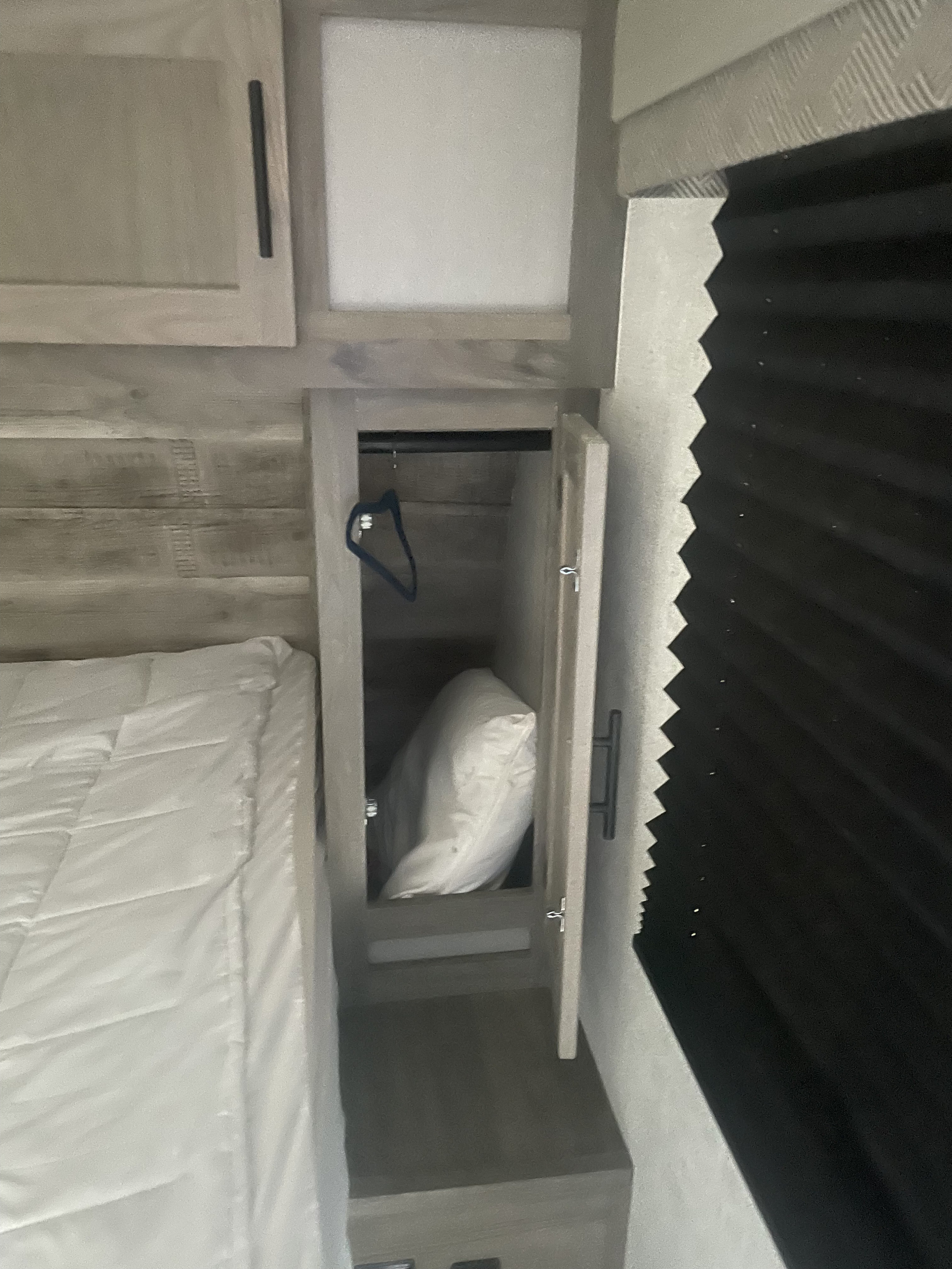 RV rental bedroom: cozy space with bed, wood cabinets, and open closet showing a pillow & hanger. Pleated blind on right.. Gulf Stream Envision 2023