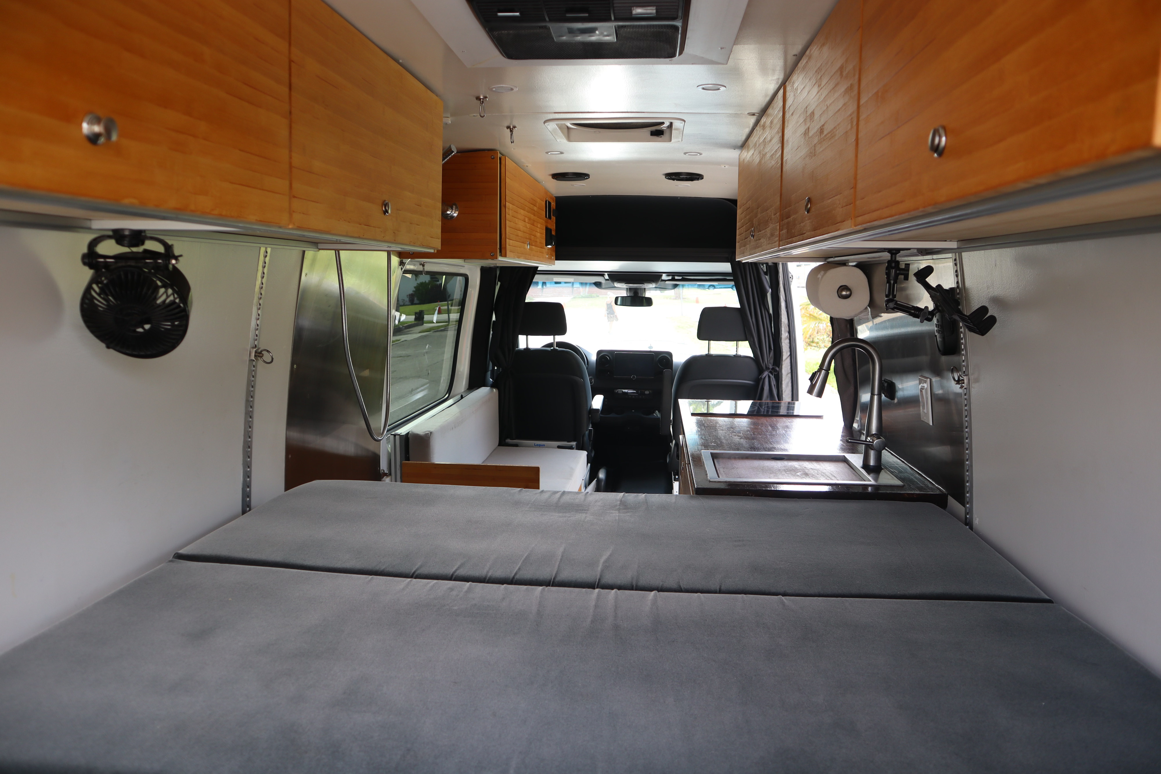 Inside an RV rental camper van: comfortable bed, kitchen sink, and wood cabinets for storage.. Mercedes-Benz Sprinter RV Motorhome Campervan 2020