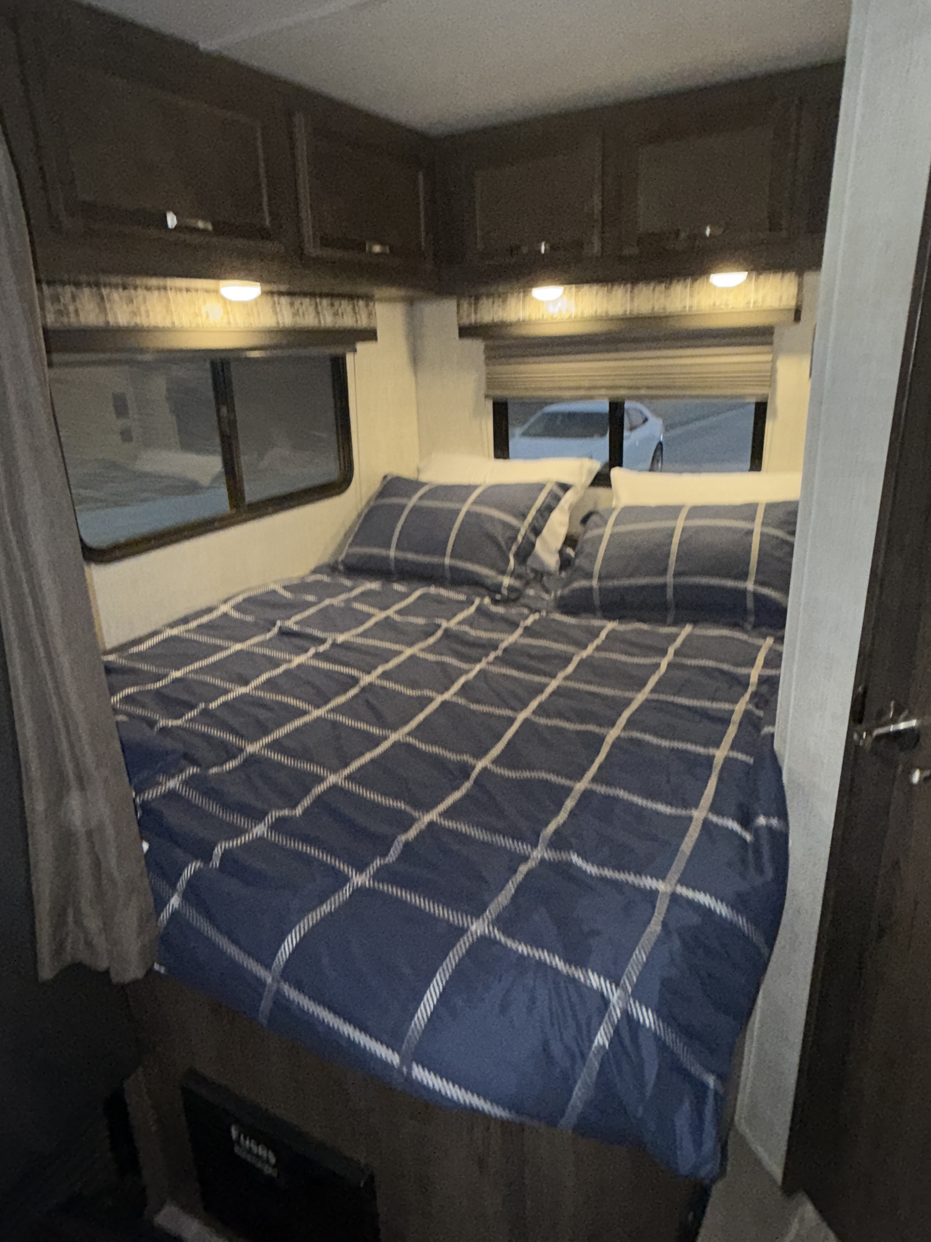 Experience comfort in this RV rental's bedroom. Features include a plaid bed, windows, and convenient overhead cabinets.. Gulf Stream Conquest 2023