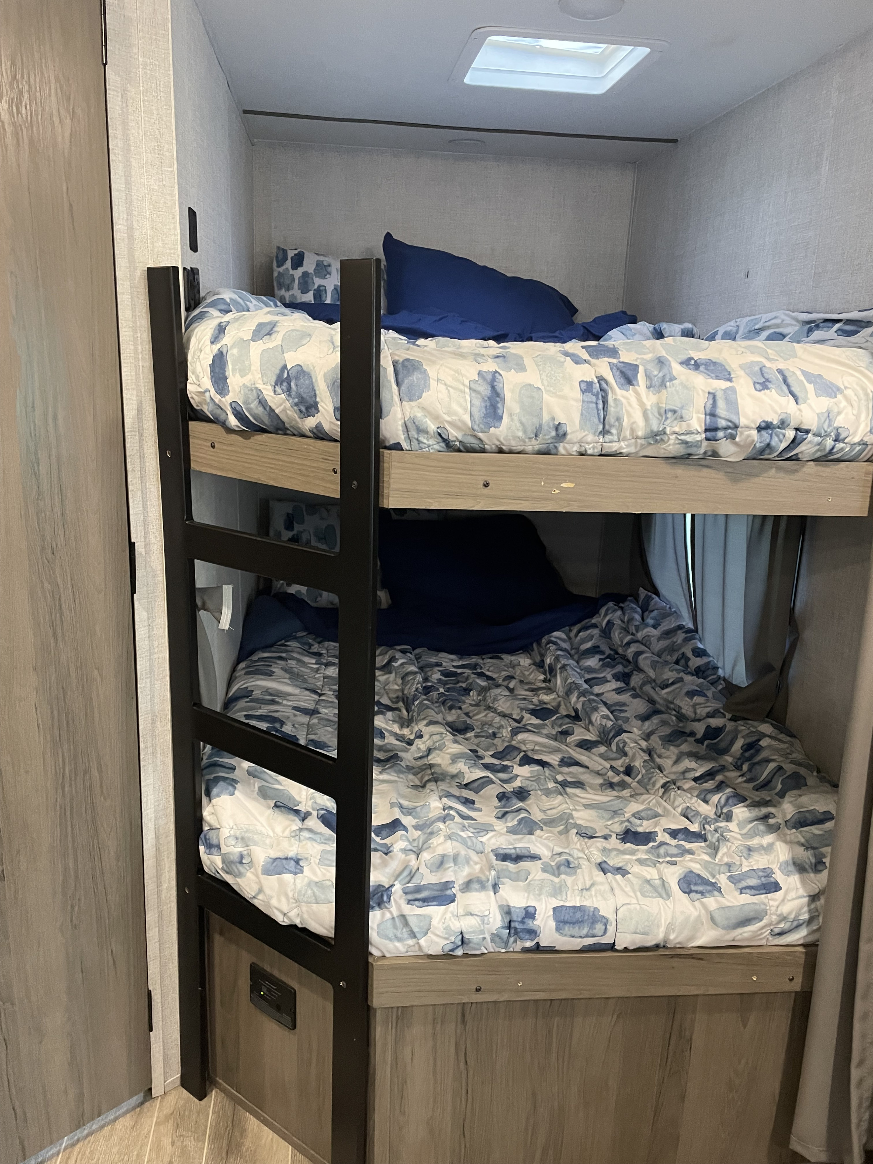 Cozy bunk beds in an RV rental, complete with blue & white bedding & pillows. Features light wood accents & a skylight.. Gulf Stream Enlighten 2021