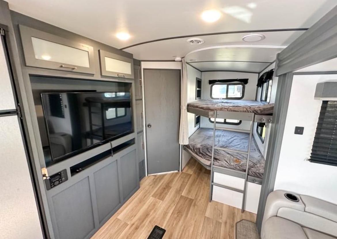 Modern RV rental interior features an entertainment center with TV, cozy bunk beds with windows, and wood flooring.. Keystone RV Bullet Ultra Lite 2023