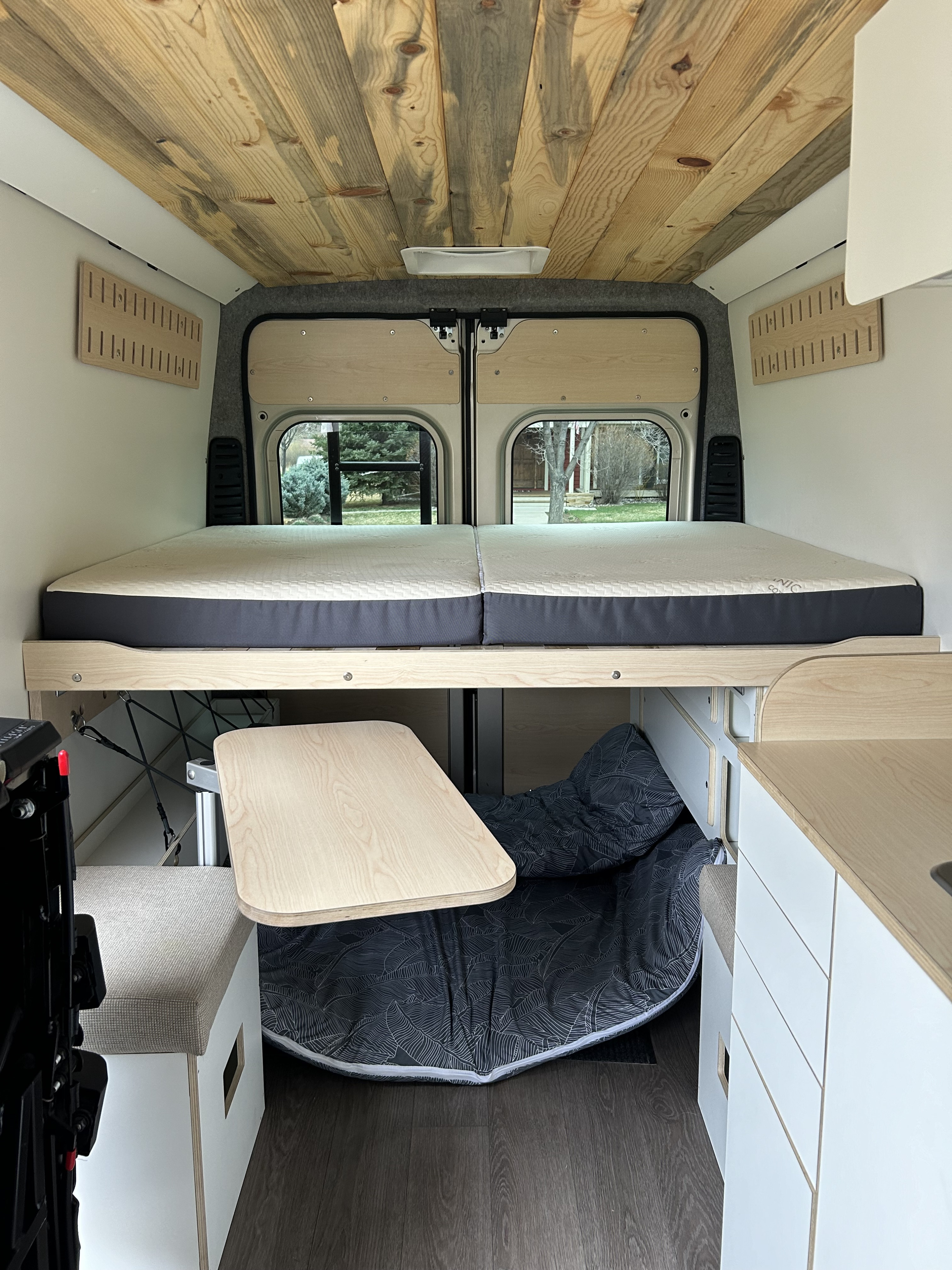 RV rental interior featuring a wooden ceiling, raised bed, and a convertible living space with a table and storage.. Dodge Pro master 2023
