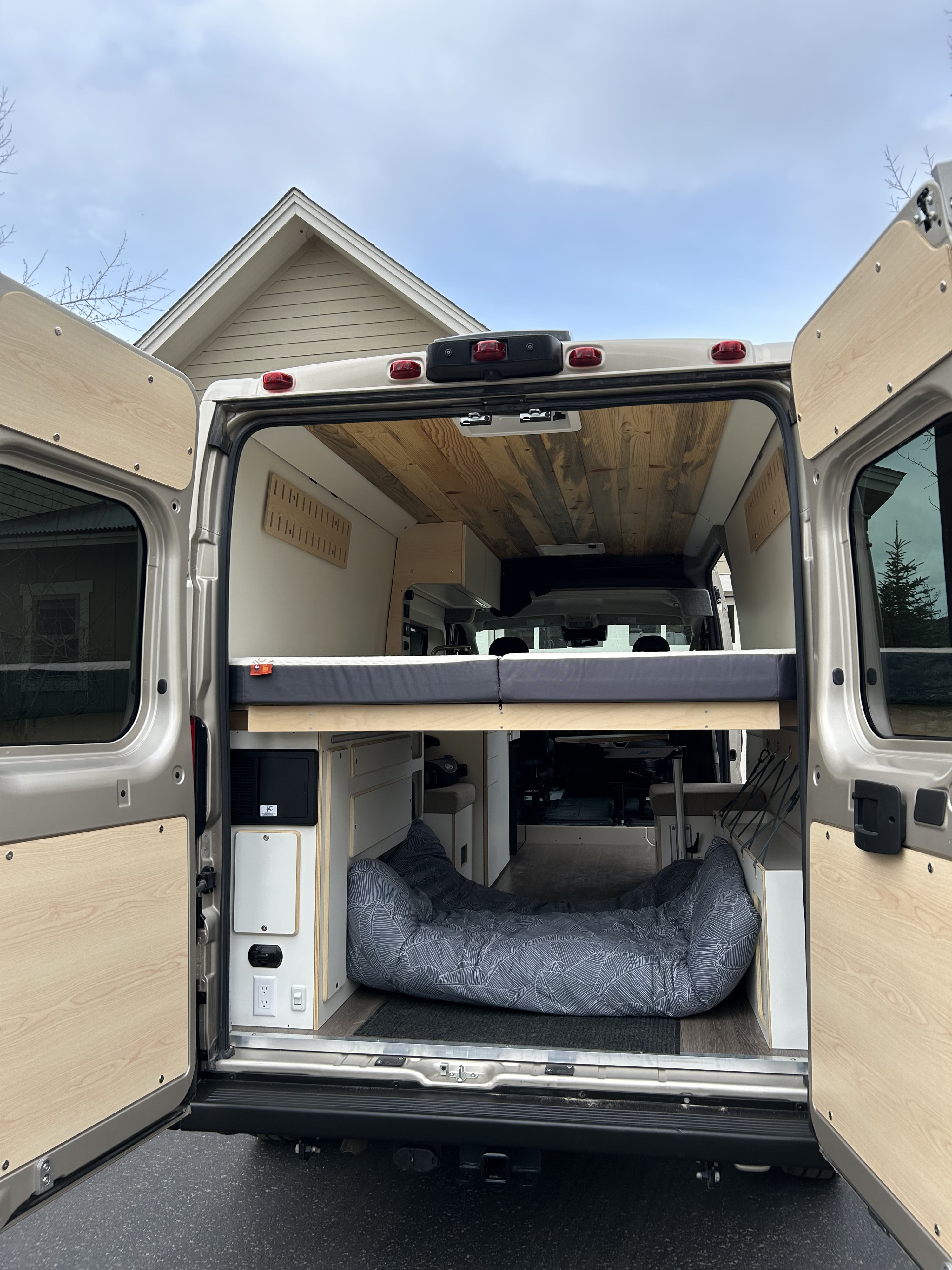 Rear view of an RV rental van conversion: a raised bed, storage, and a dog bed on the floor. Ready for adventures!. Dodge Pro master 2023