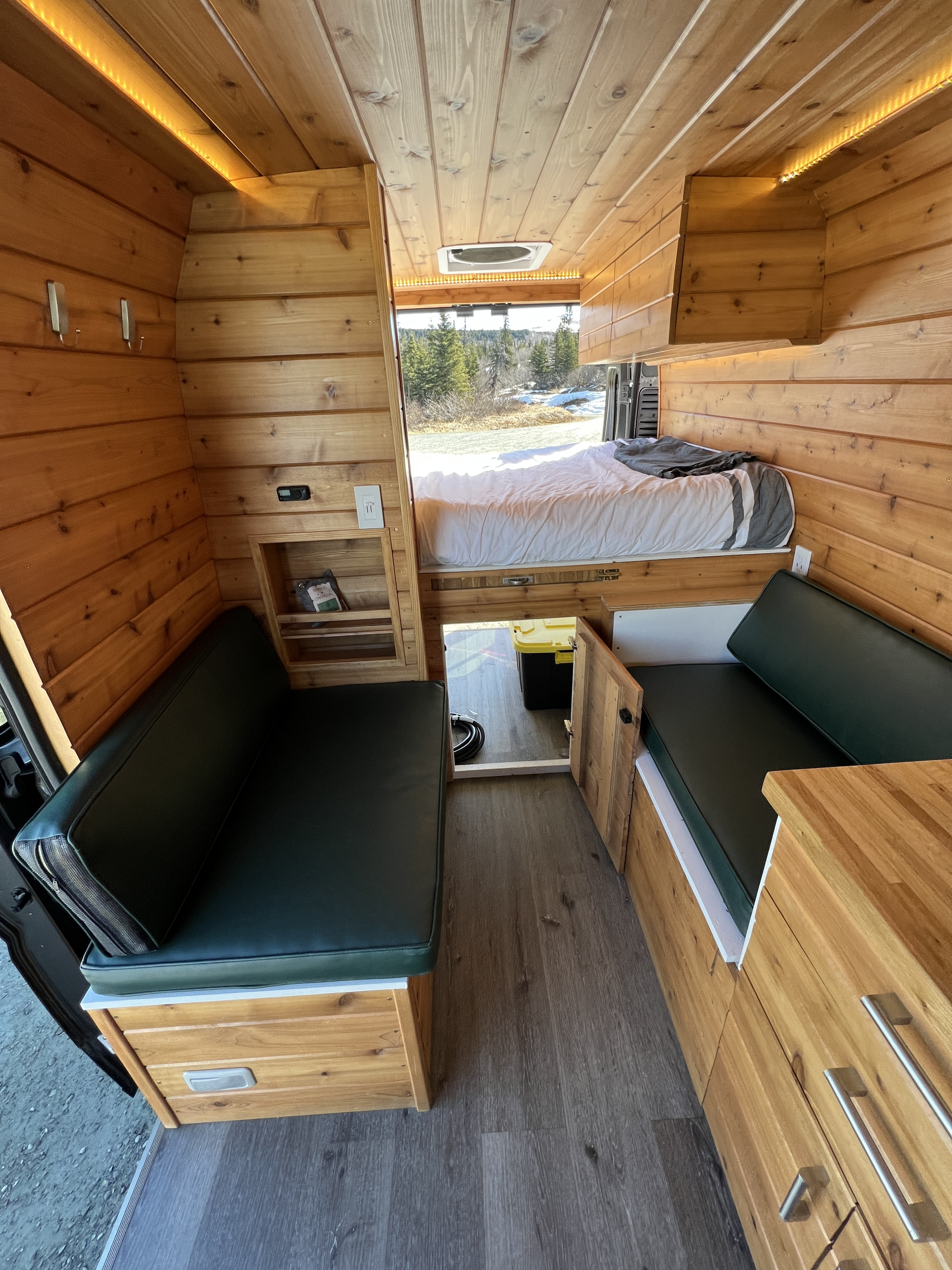 Inviting wooden RV rental interior with bed, built-in seating, and storage. Ideal for adventurers.. Dodge Van 2024