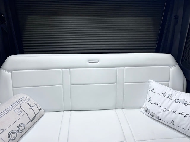 RV rental interior: a clean white bench seat with decorative travel pillows against a dark pleated window blind. Ready for adventure!. Airstream Interstate 2020